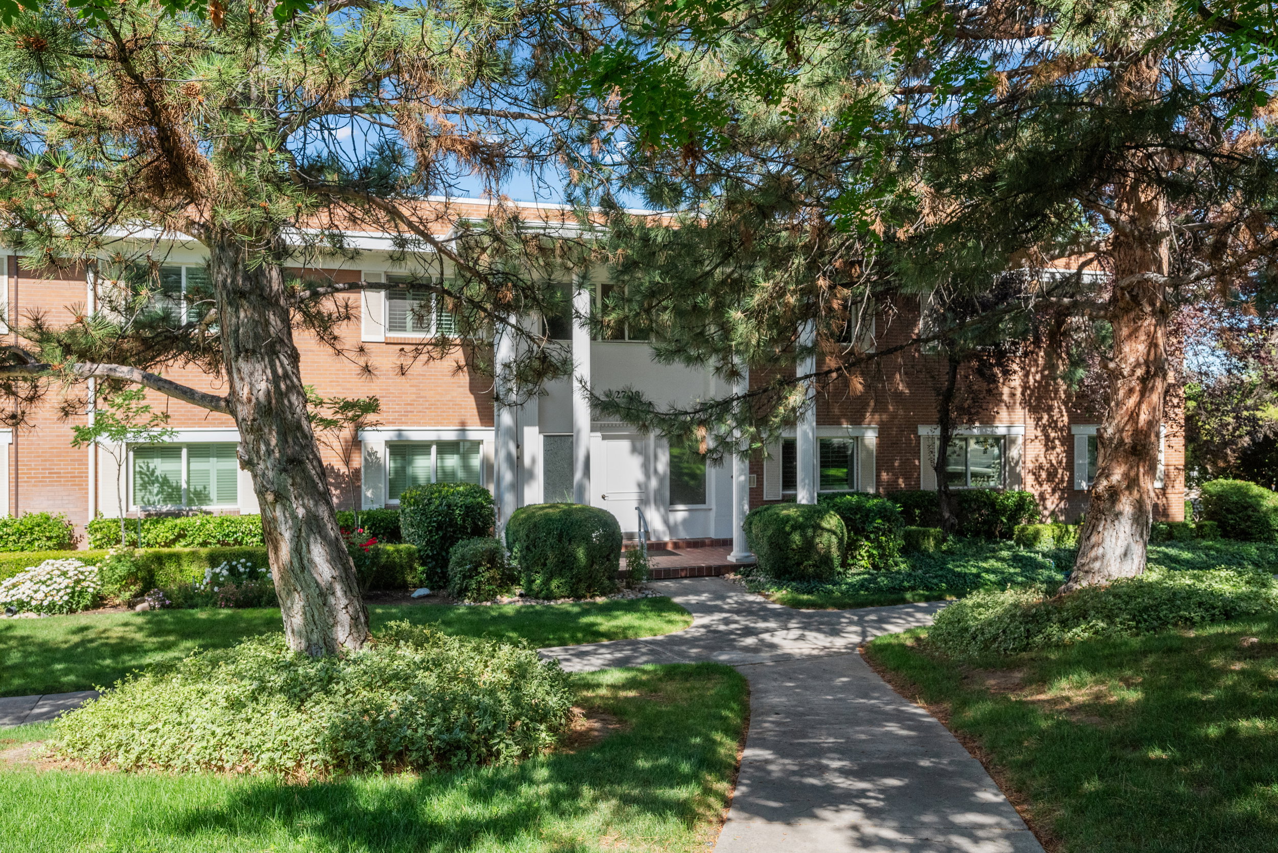 Brick facade residence featuring white trim, a covered entryway with white columns, and a concrete pathway
