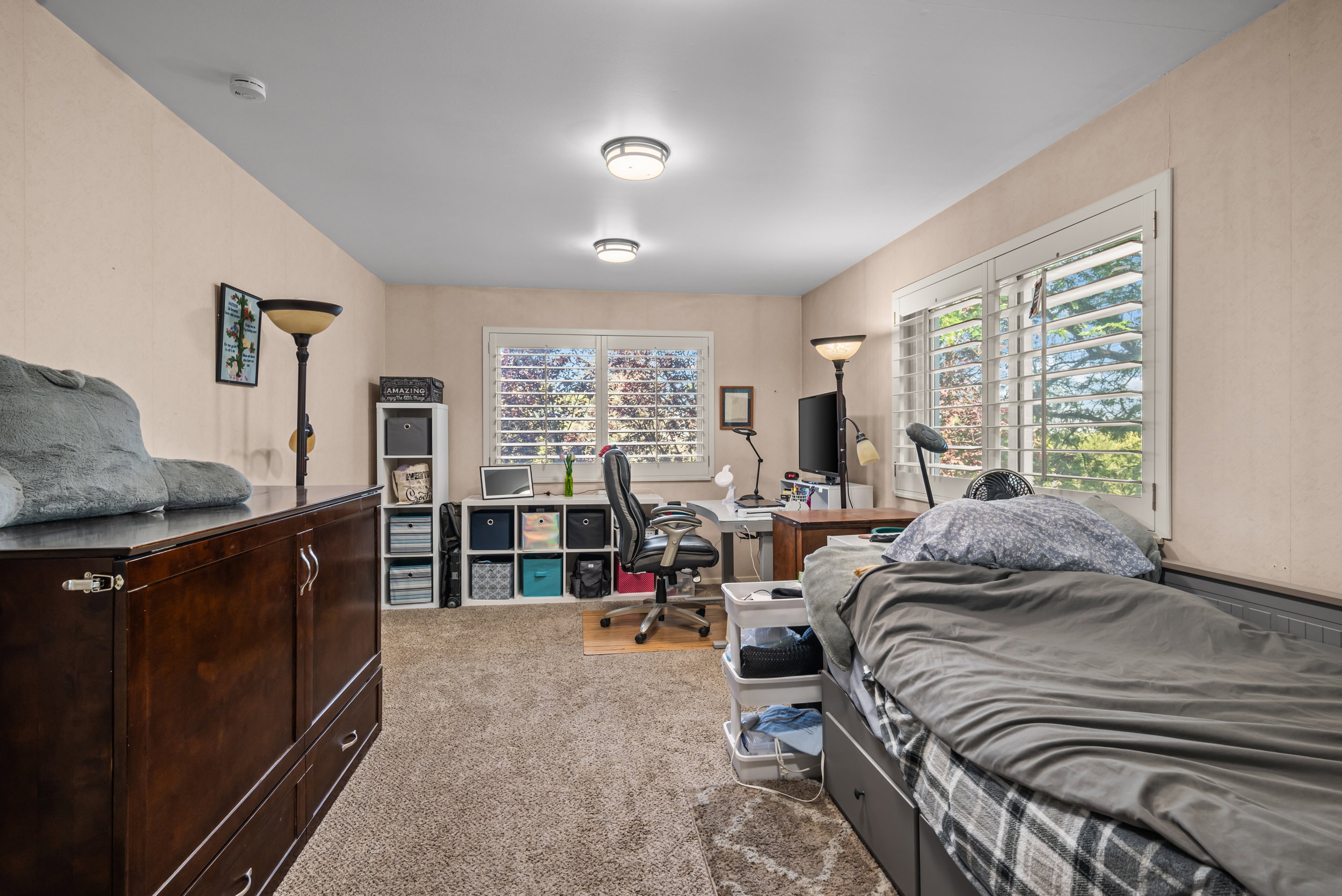 Carpeted room featuring multiple windows with louvered shutters, flush-mount ceiling lighting, and a neutral wall finish