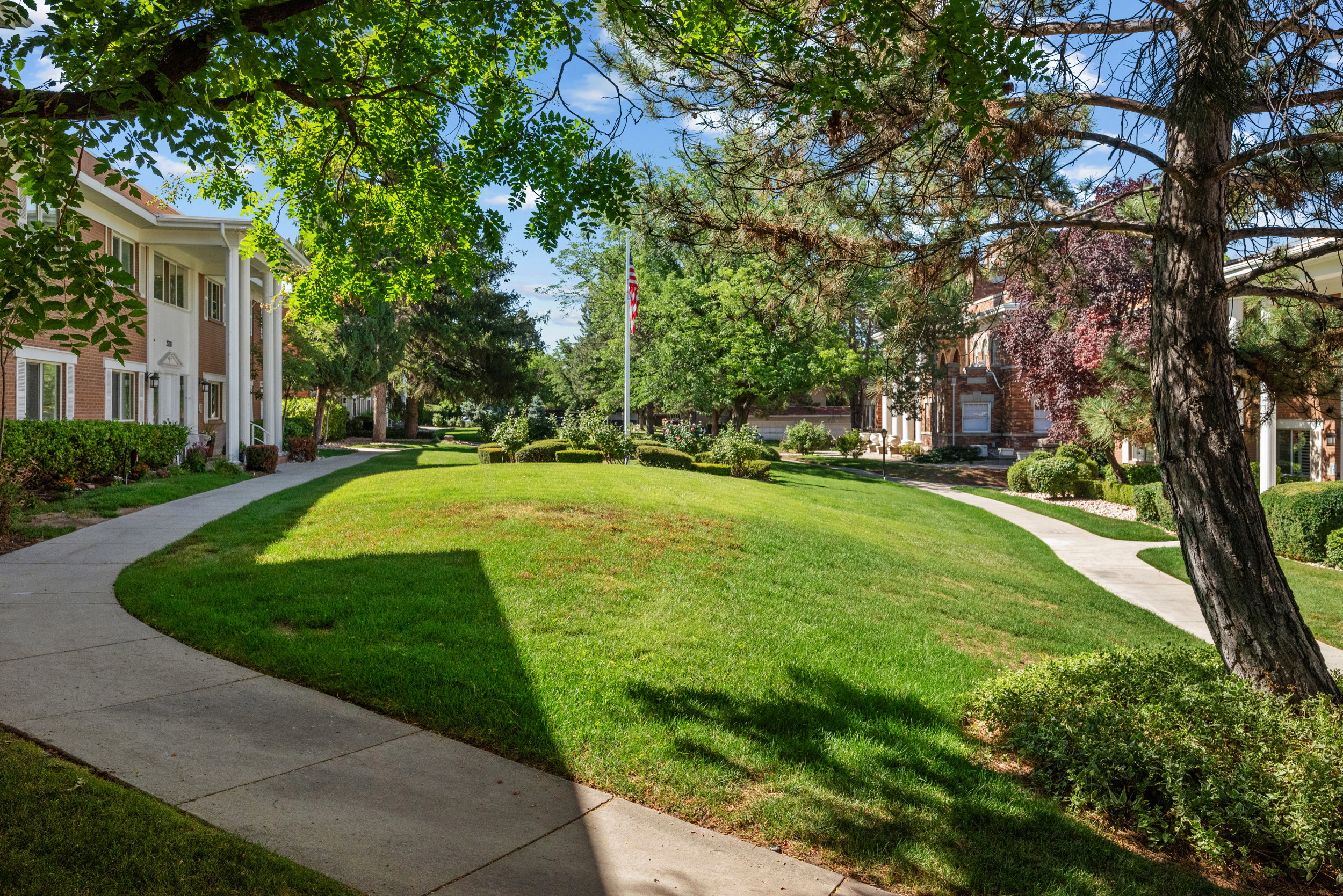 Manicured green spaces featuring mature trees and shrubs, bordered by paved walkways