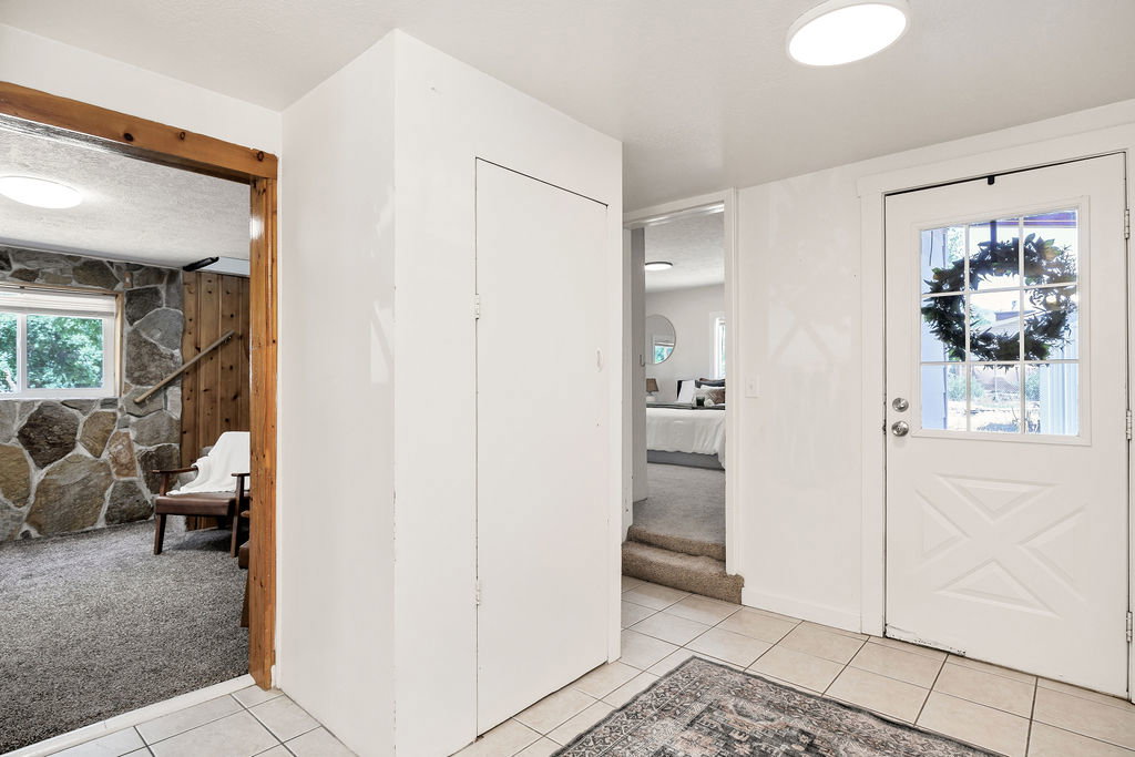 Tiled entryway leading the carport, featuring a paneled door with glass insert, flush-mount ceiling lighting, and a 2 storage closets.