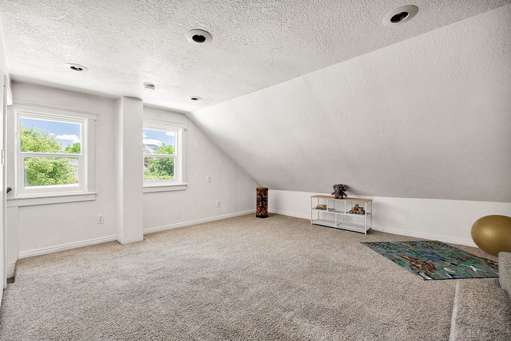 Spacious room featuring sloped ceilings, recessed lighting, and soft gray carpeting