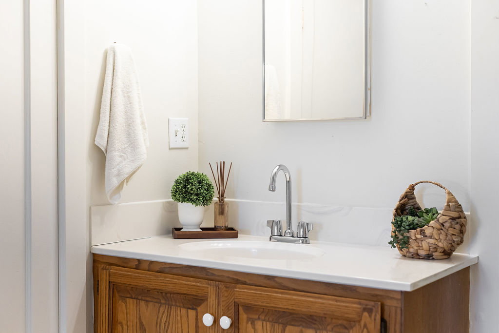 Bathroom vanity featuring a light-toned countertop with integrated sink, chrome faucet, and wood-finish cabinetry with white knobs