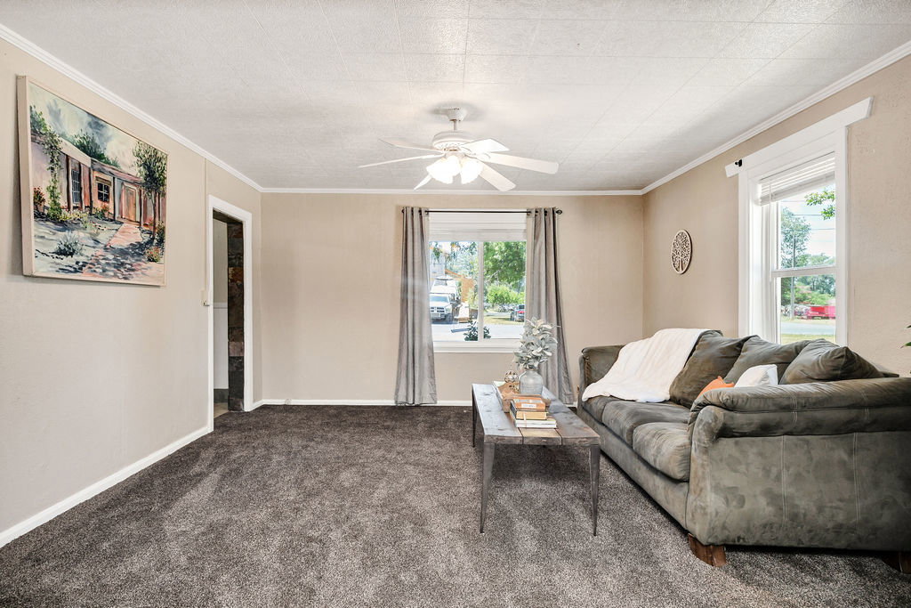 Carpeted living space featuring neutral wall tones, white trim, and a ceiling fan with light fixture
