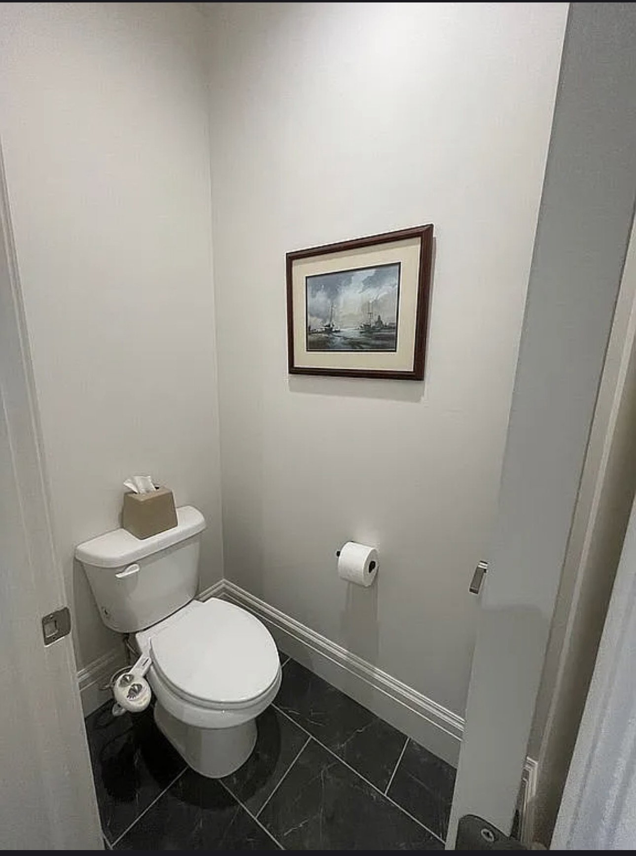 Powder room featuring a white toilet with bidet attachment, dark gray tile flooring, and light gray wall paint