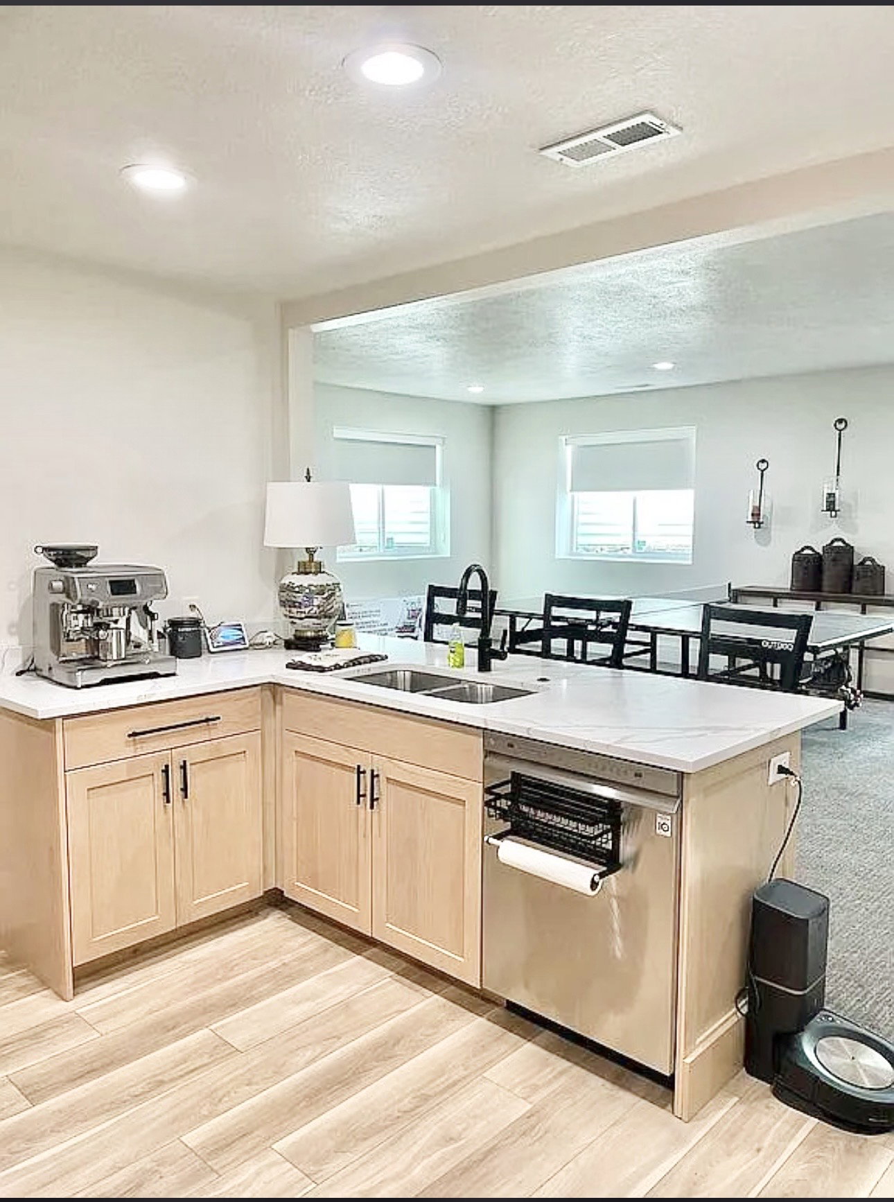 Kitchenette featuring light wood-finish cabinetry, white countertops, and a double basin stainless steel sink with a matte black faucet