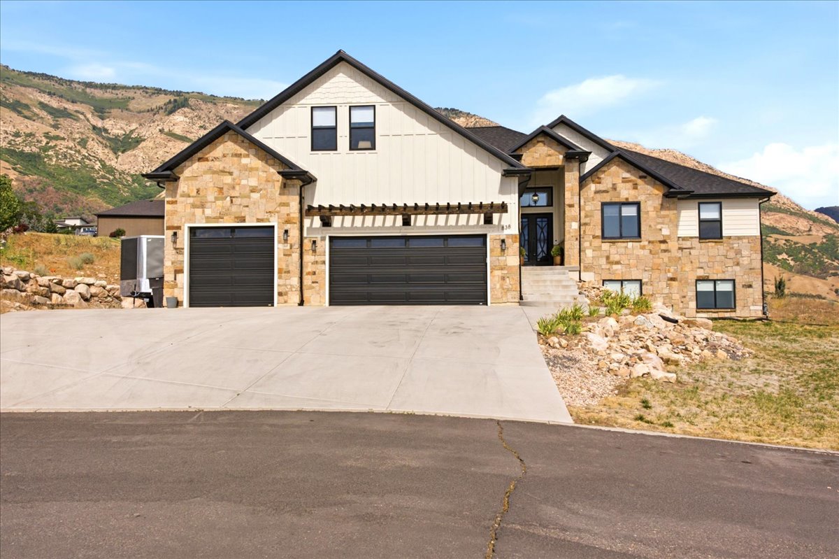 Custom home featuring a stone and vertical siding facade, dark trim, and a prominent two-car garage with modern doors
