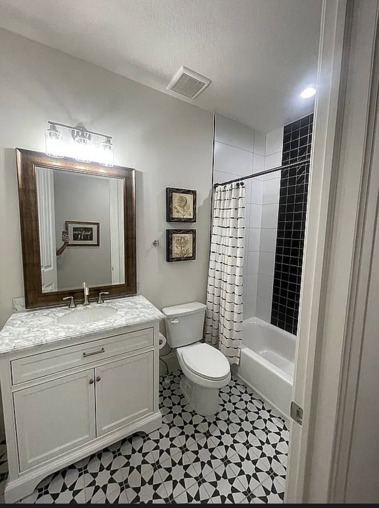 Bathroom featuring a patterned black and white floor, a white vanity with a light-colored countertop, and a shower/tub combination with black subway tile accents