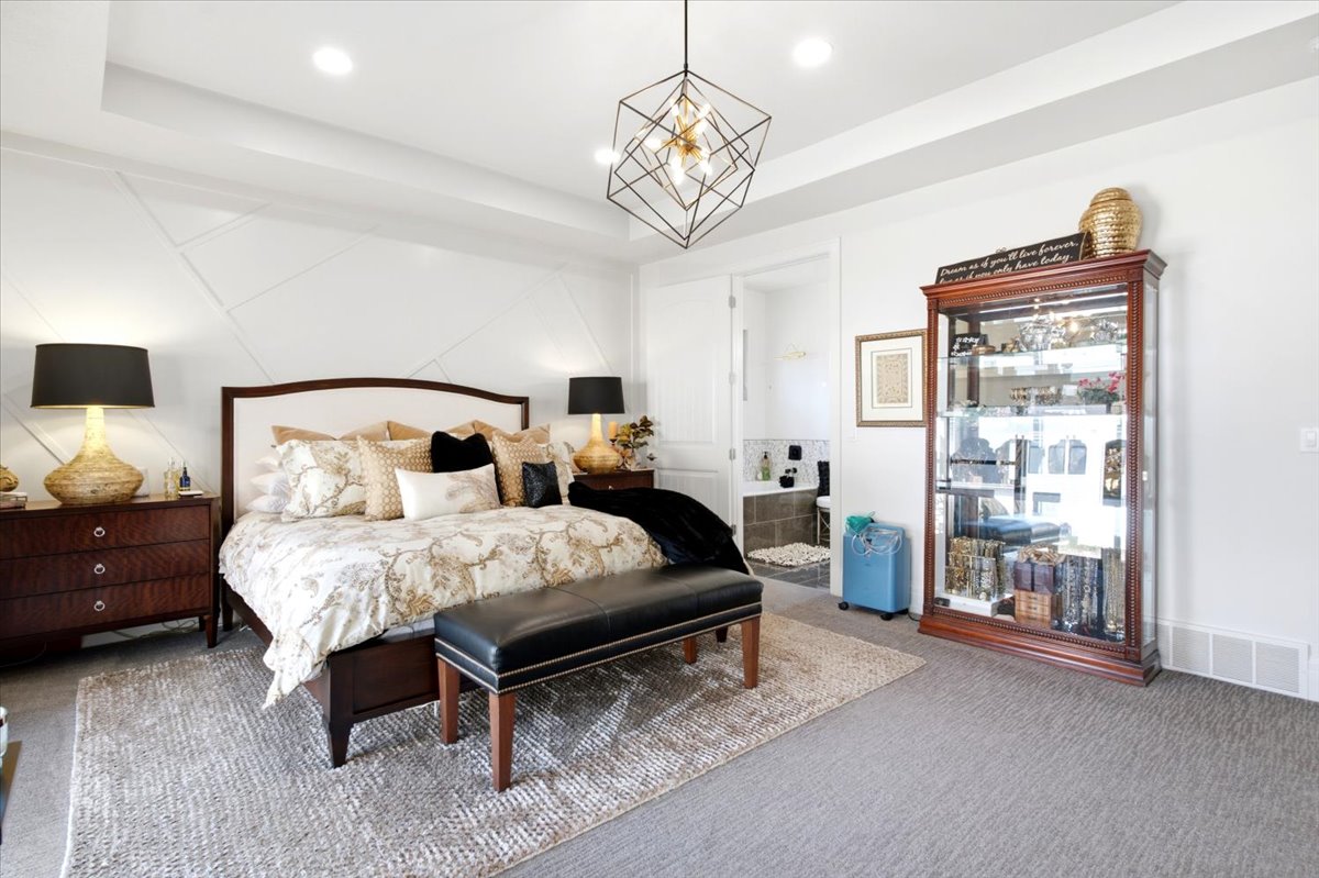Spacious bedroom featuring textured accent wall paneling, a recessed tray ceiling, and a modern geometric pendant light fixture