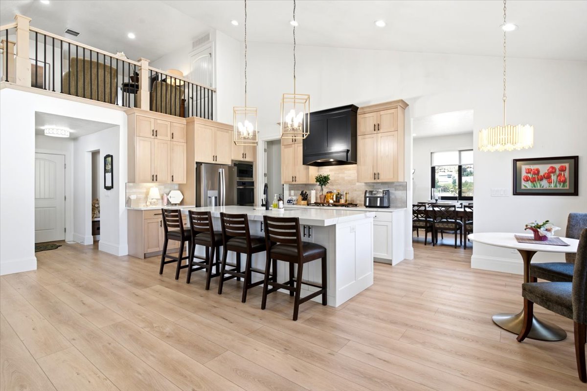 Spacious kitchen featuring light wood-finish flooring, a central island with countertop seating, stainless steel appliances, light-toned cabinetry, and an overhead loft area