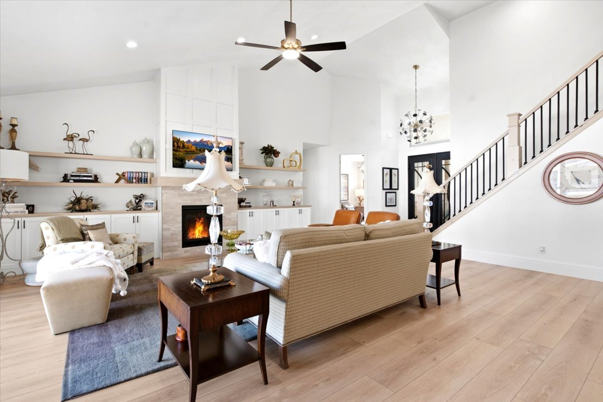 Vaulted living space featuring a fireplace with stone surround, custom built-in cabinetry, and wood-finish flooring