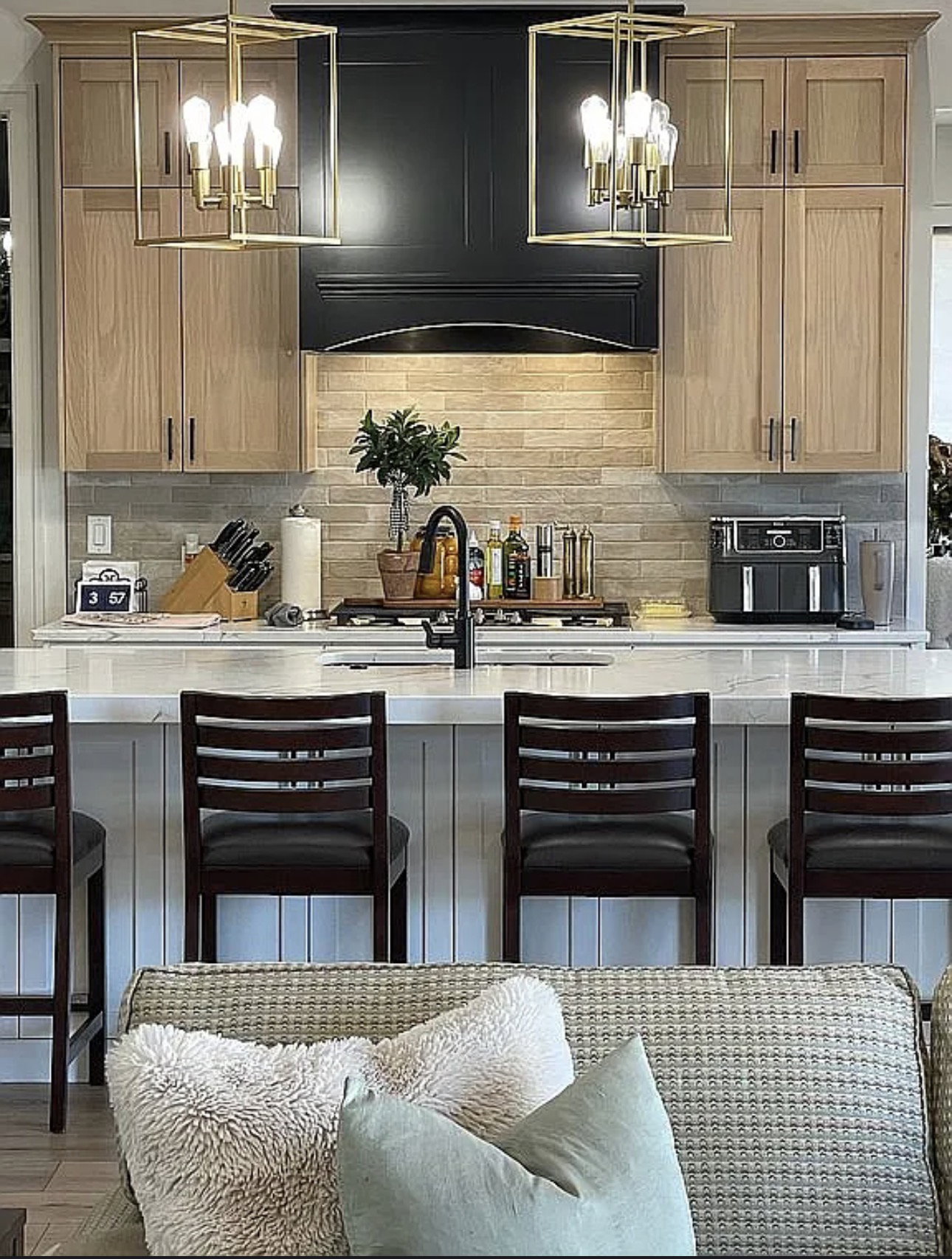 Kitchen featuring natural wood-finish cabinetry, a black range hood, and a light-toned brick-patterned backsplash