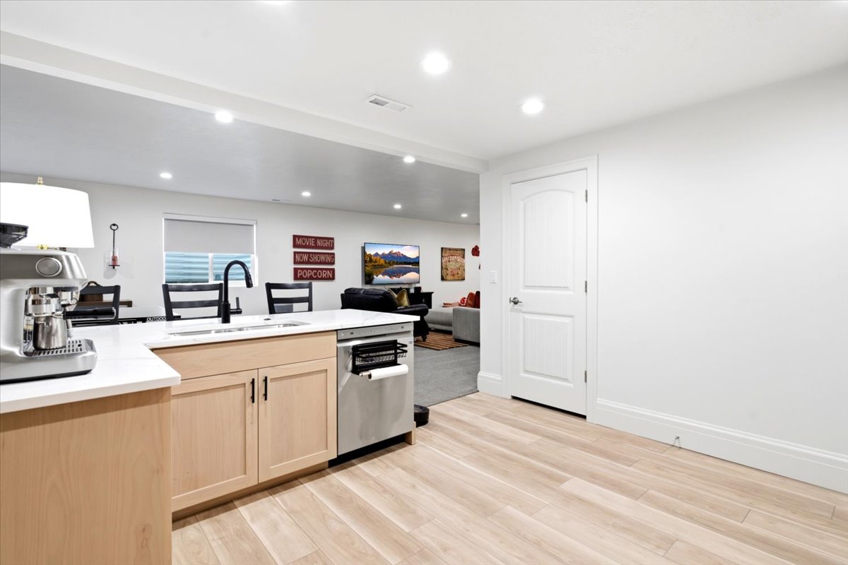 Kitchenette featuring light wood-finish cabinetry, a white countertop, stainless steel sink with a matte black faucet, and a stainless steel dishwasher