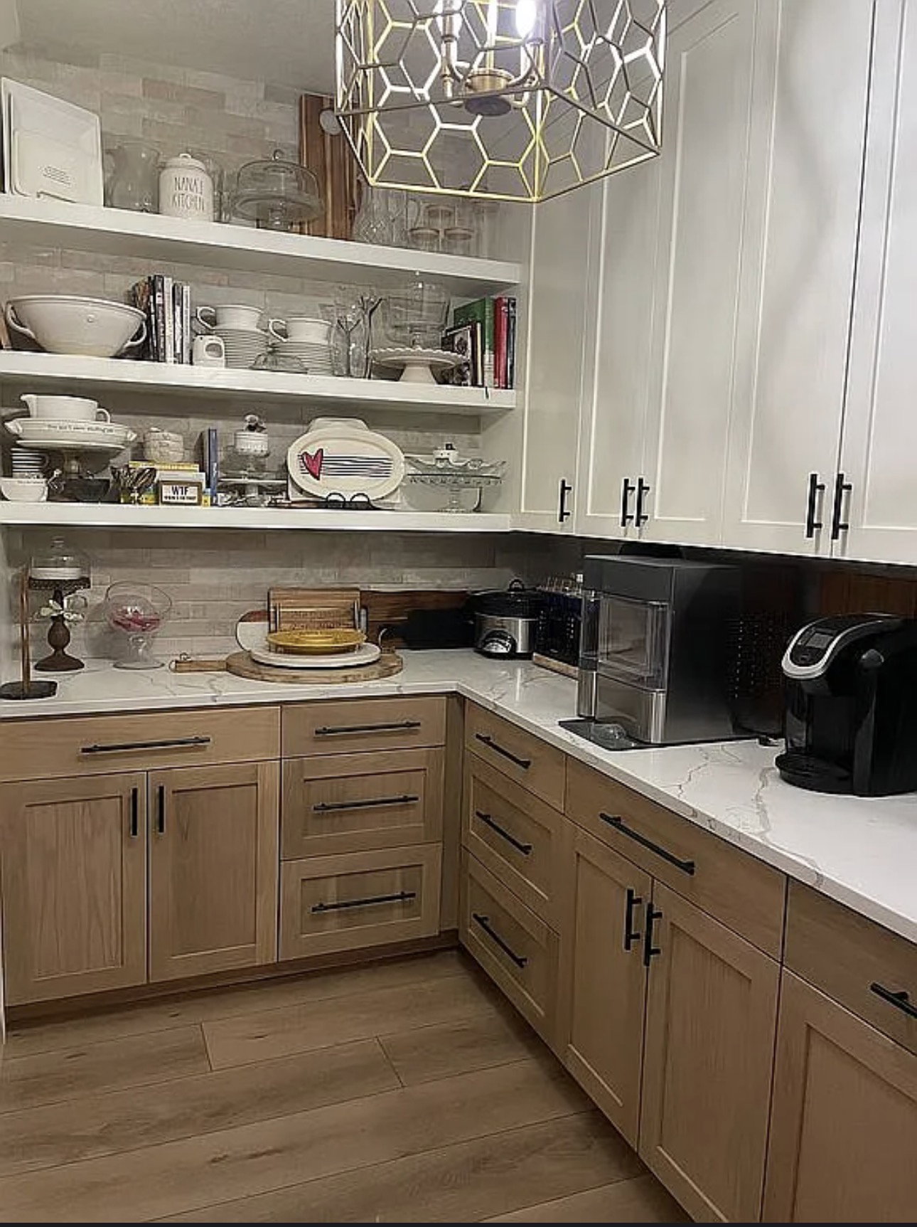 Kitchen featuring a geometric pendant light, white upper cabinetry, natural wood-finish lower cabinetry, light-toned countertops, and open shelving with tile backsplash