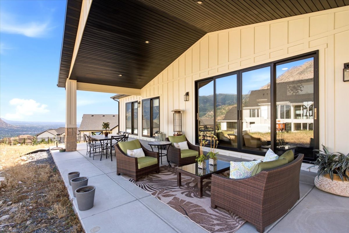 Expansive covered patio featuring a concrete surface, board and batten siding, black soffit, and multiple large sliding glass doors