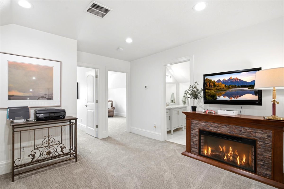Carpeted room featuring a built-in electric fireplace with stone-look surround and wood-finish mantel, white walls, and recessed lighting