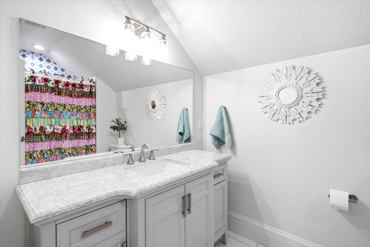 Bathroom featuring a single vanity with a light-toned countertop, an integrated sink, and brushed nickel fixtures