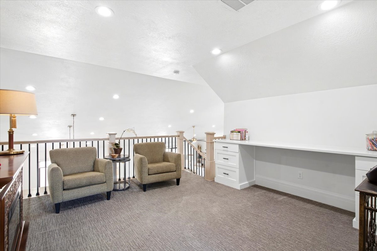 Spacious loft area featuring a built-in white desk with drawers, recessed lighting, and a neutral carpeted floor