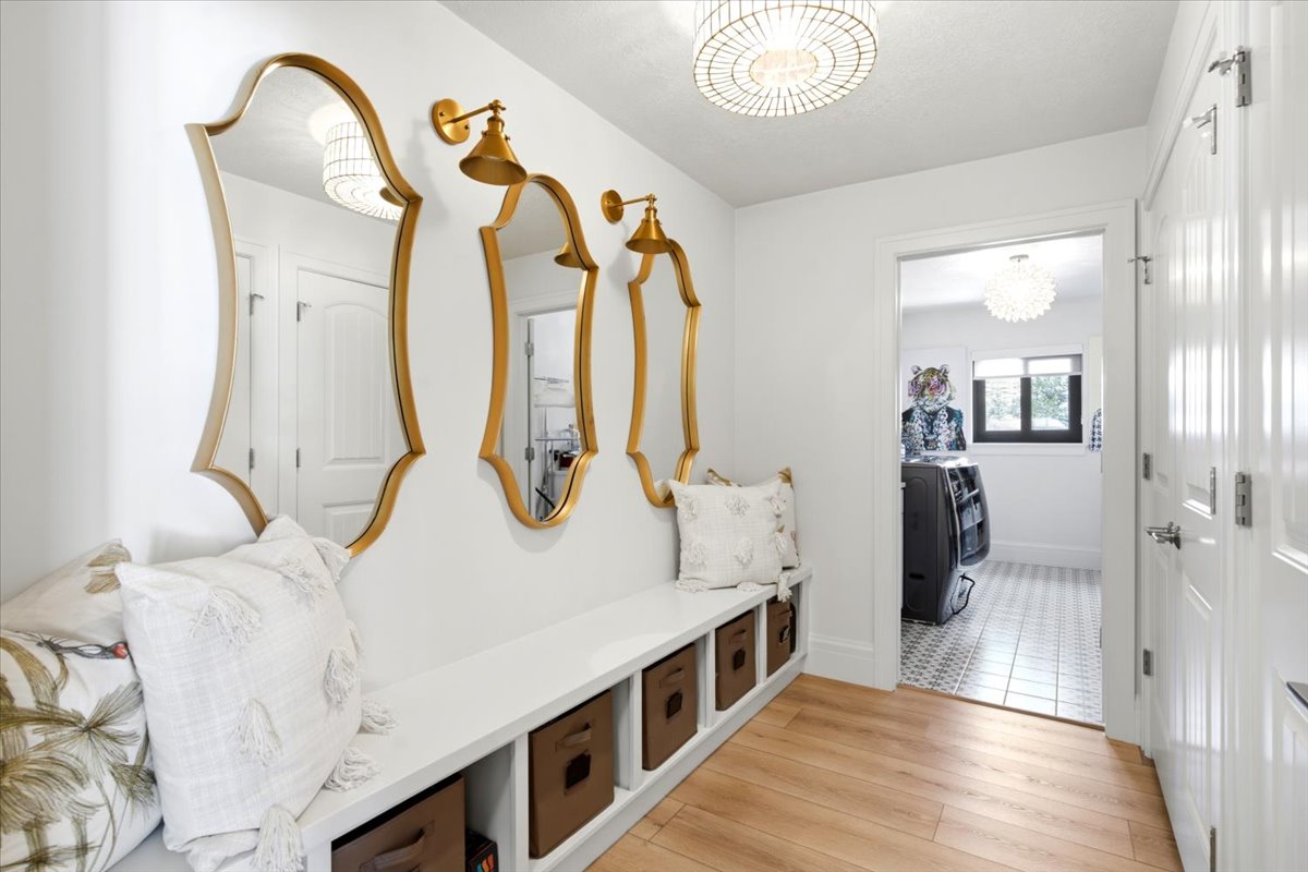 Entryway featuring wood-finish flooring, a built-in bench with integrated cubby storage, and three decorative gold-framed mirrors with coordinating wall sconces