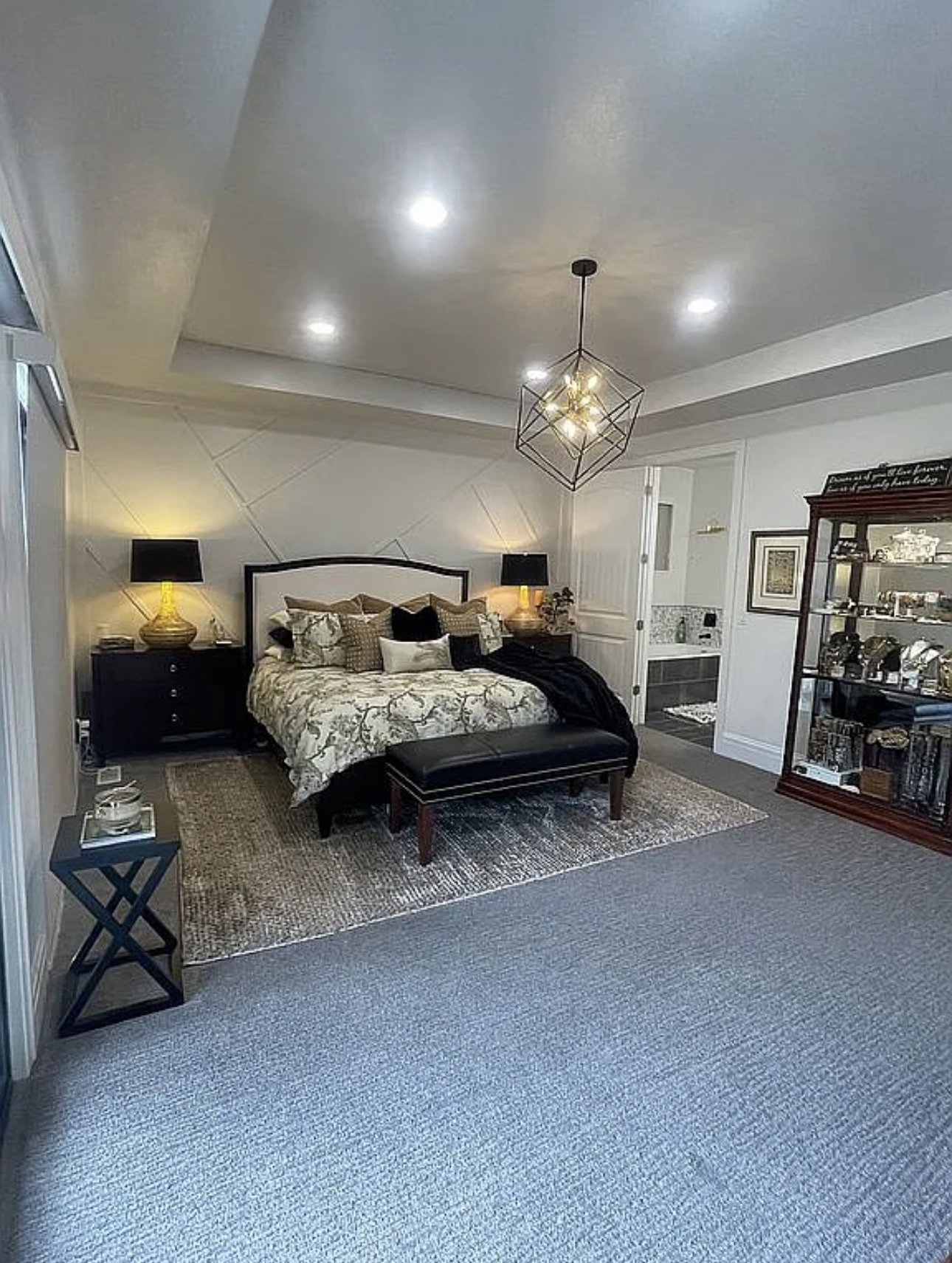 Recessed ceiling lighting, a geometric pendant light fixture, and a tray ceiling illuminate this carpeted room