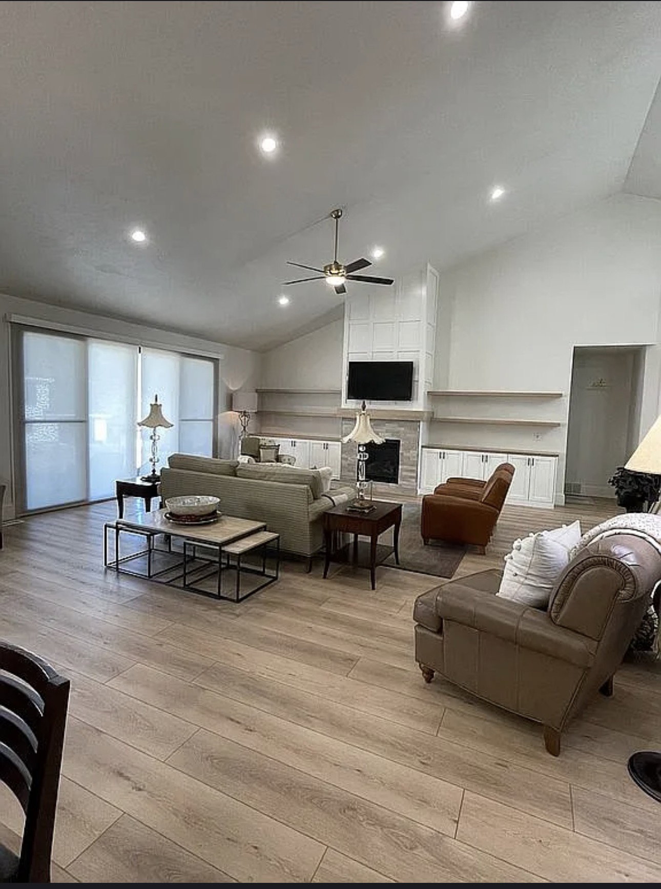Spacious living area featuring wood-finish flooring, a vaulted ceiling with recessed lighting and a ceiling fan, and large sliding doors
