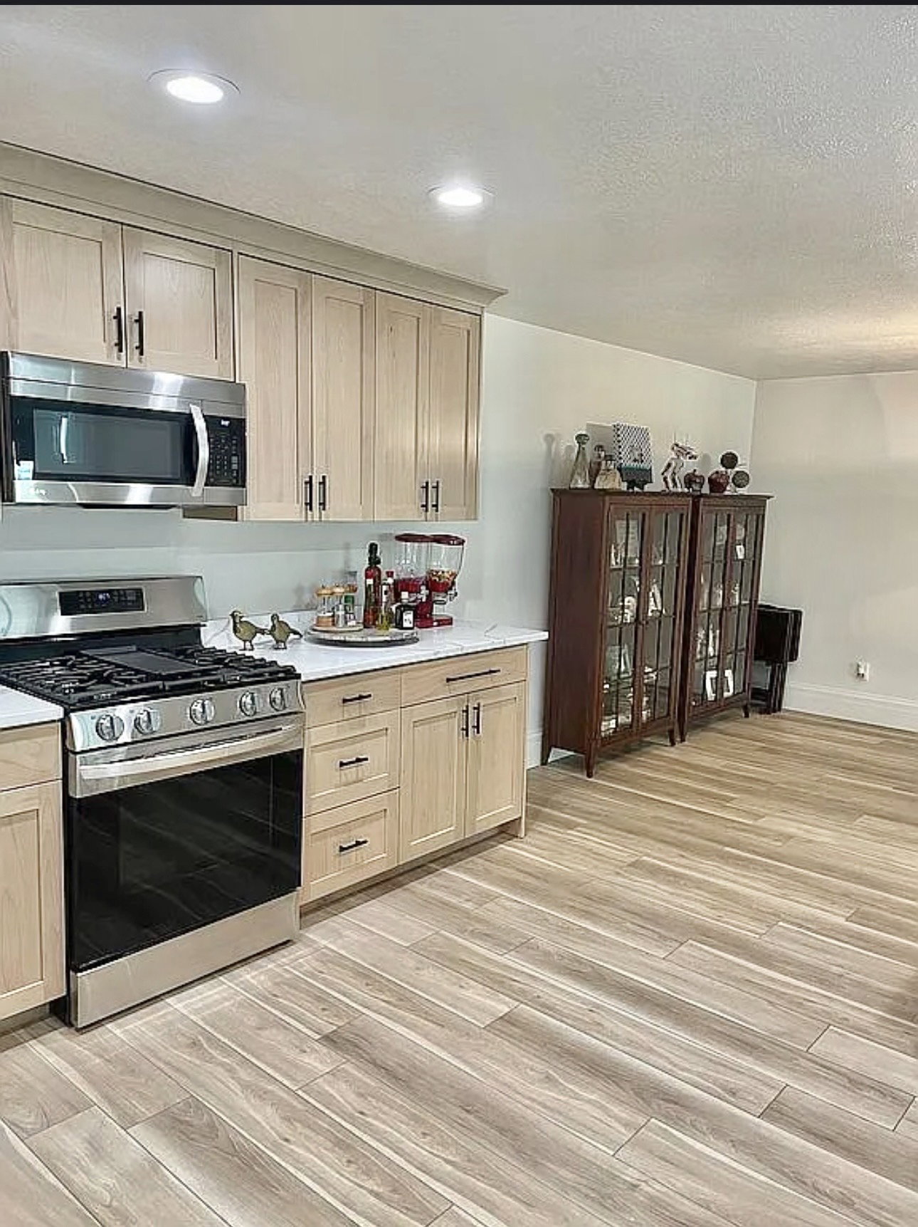 Modern kitchen featuring light wood-finish cabinetry, stainless steel range and microwave, white countertops, recessed lighting, and wood-look plank flooring