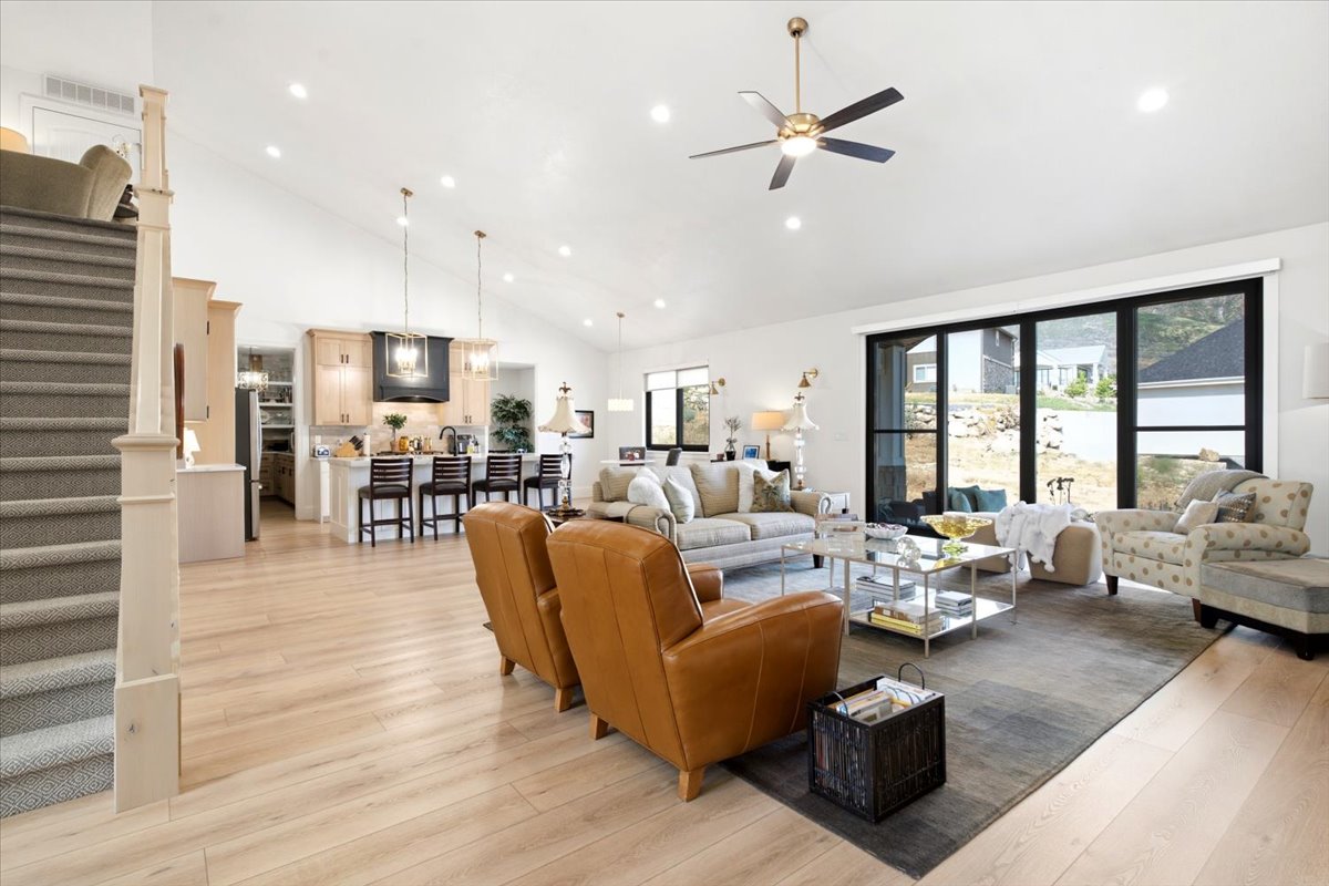 Spacious living area featuring light wood-finish flooring, vaulted ceilings with recessed lighting, and a modern ceiling fan