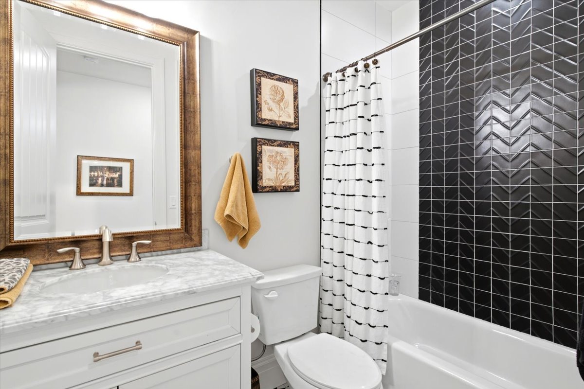 Bathroom featuring a white vanity with an integrated sink and brushed nickel fixtures, a framed mirror, and a white bathtub with a black herringbone tile surround