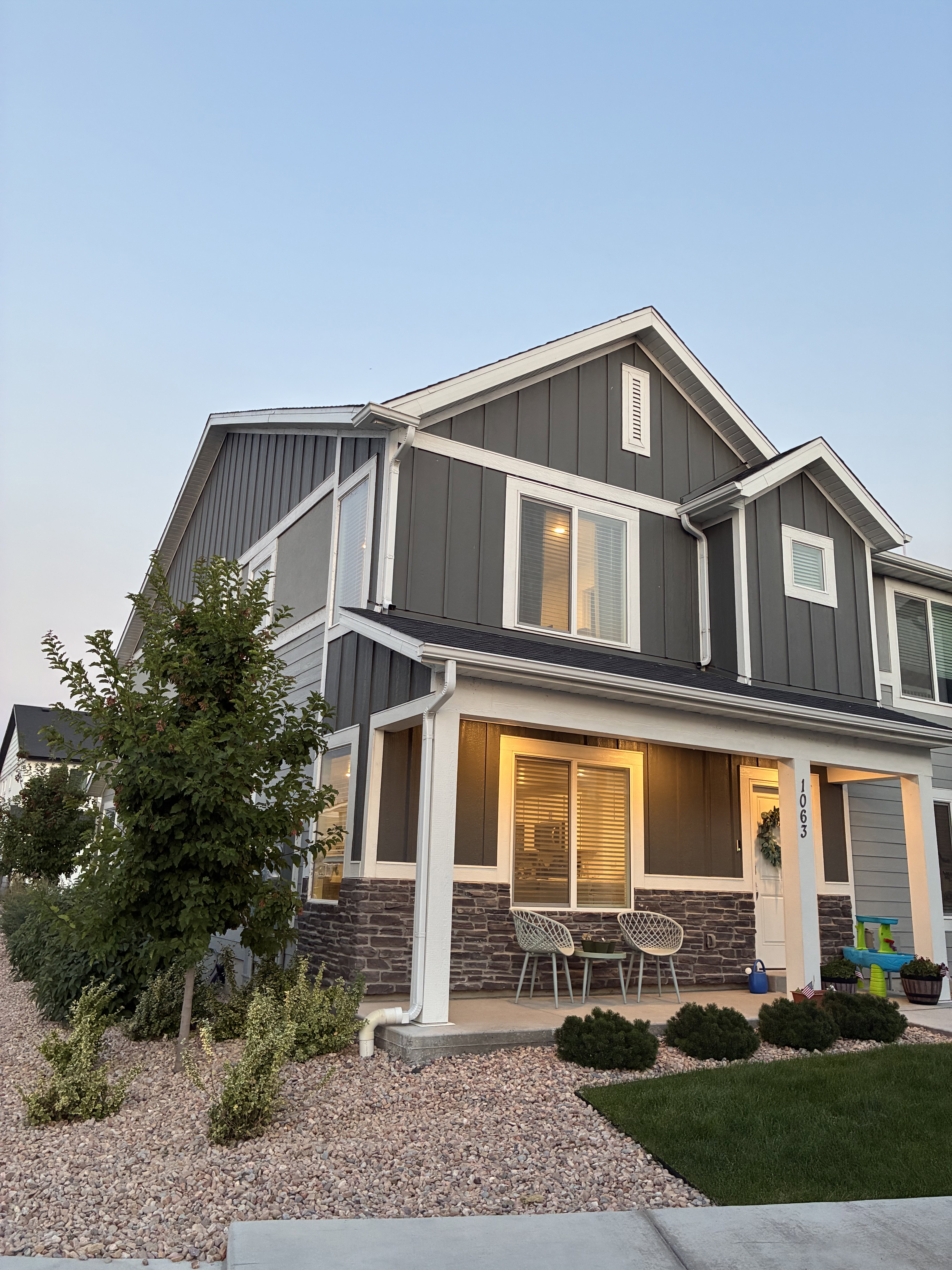 Two-story residence featuring a covered front porch with stone accents, board and batten siding, and a well-maintained lawn with decorative gravel landscaping