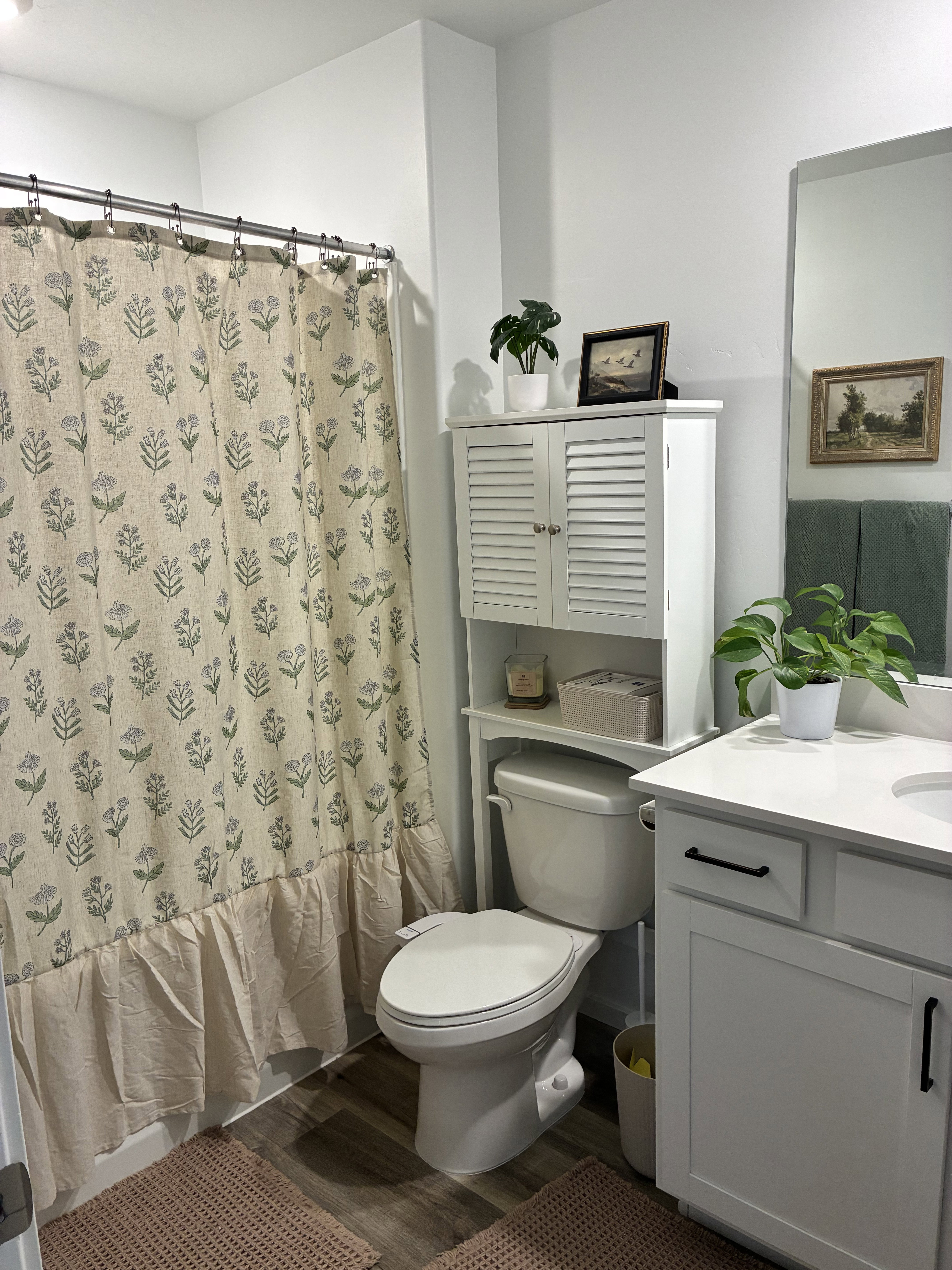 Bathroom featuring a white vanity with a quartz-finish countertop, wood-finish flooring, and a built-in over-toilet storage unit