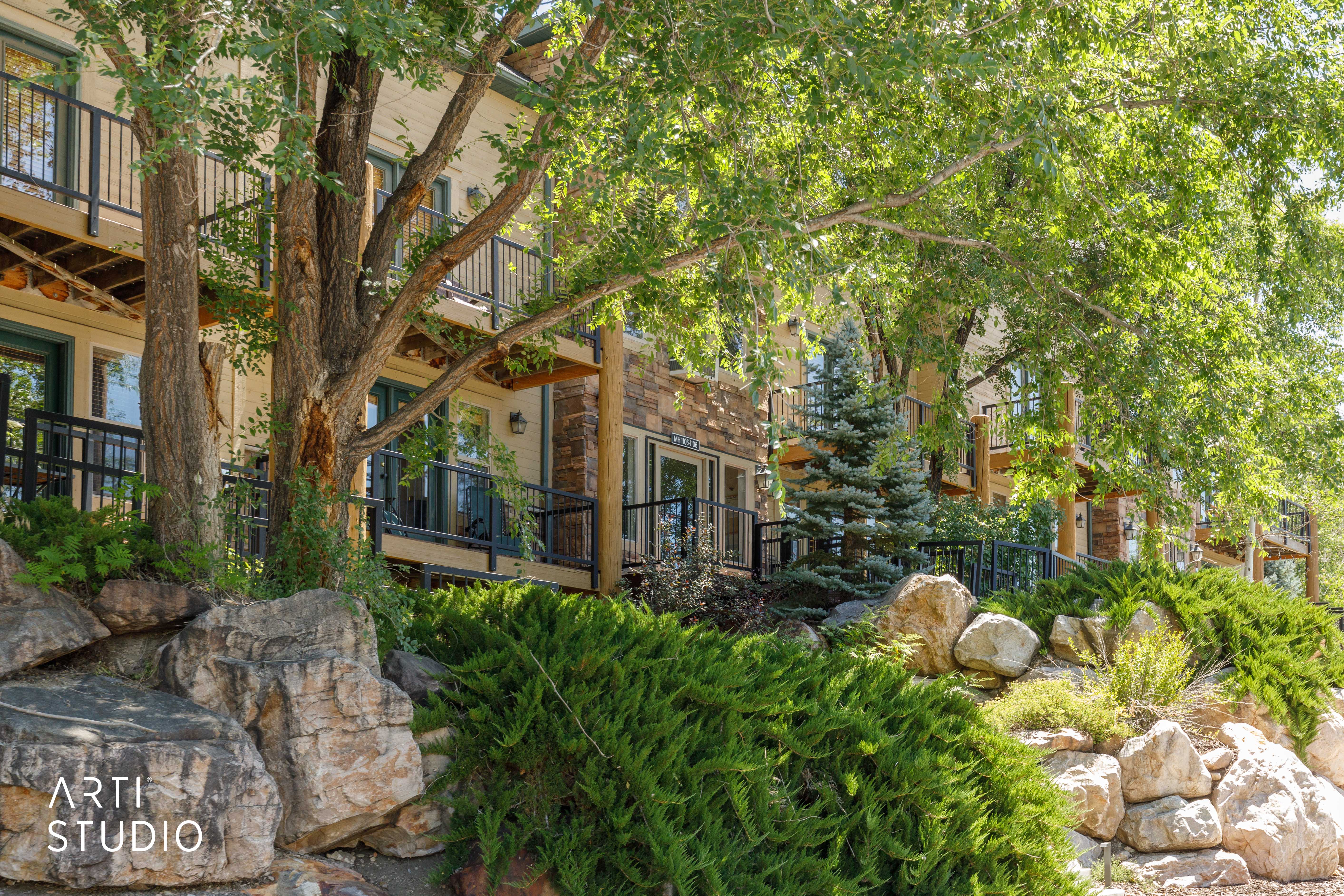 Multi-level building exterior featuring balconies with black metal railings, stone and stucco siding, and double glass doors