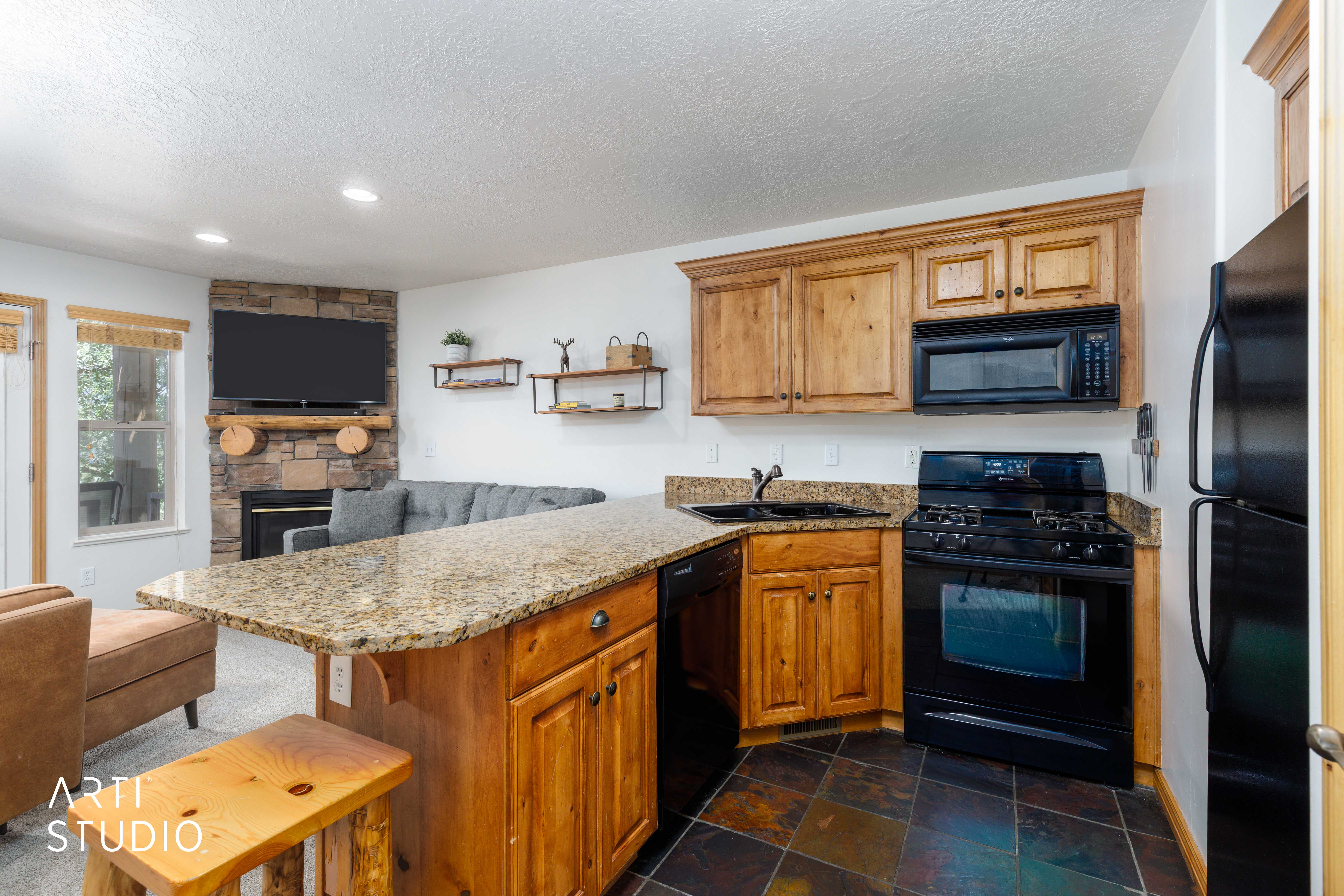 Kitchen featuring wood cabinetry, granite countertops, and black appliances, including a built-in microwave, gas range, and refrigerator