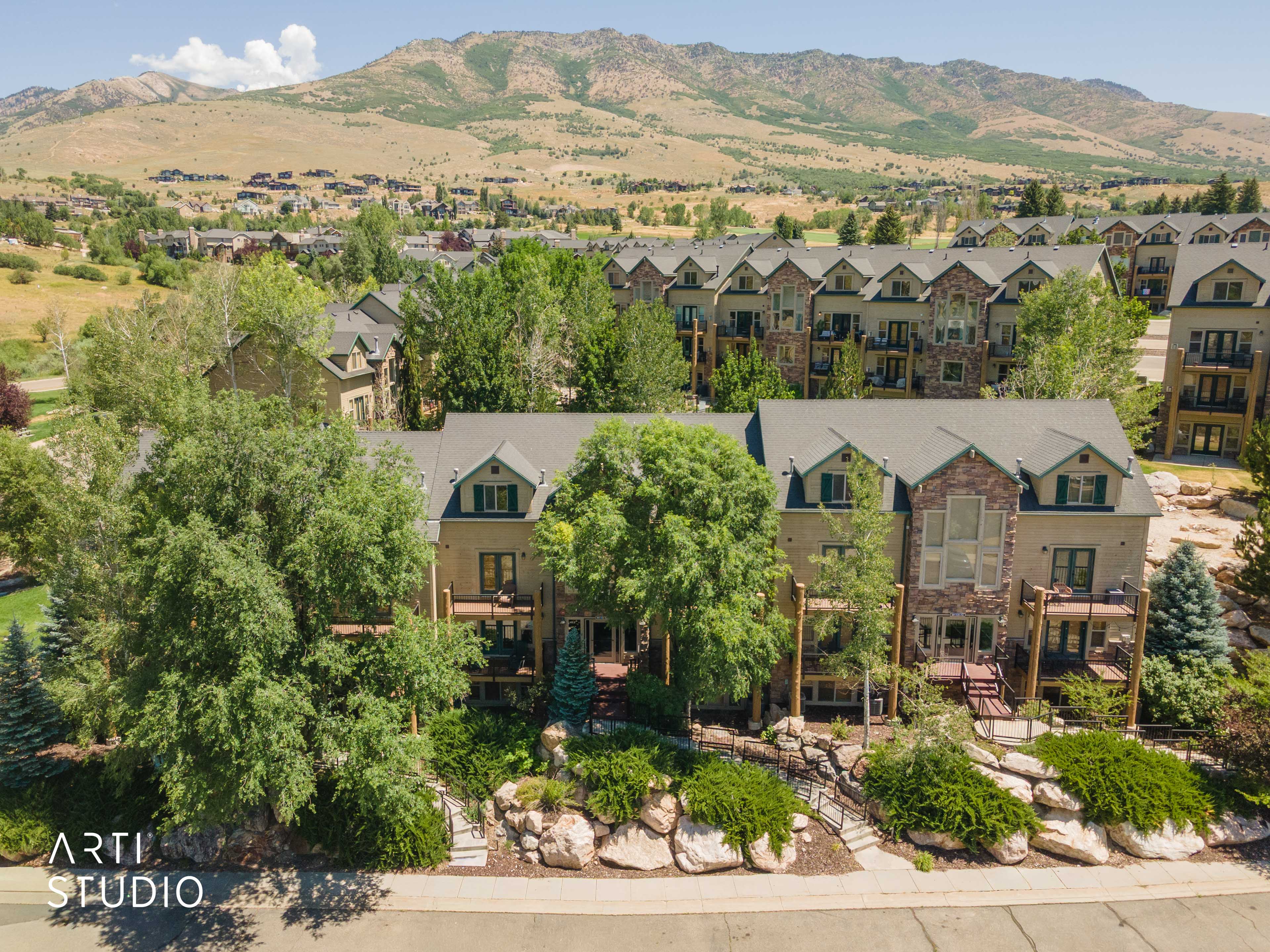 Multi-level townhome featuring a stone and stucco facade, dormer windows, multiple balconies, and mature landscaping