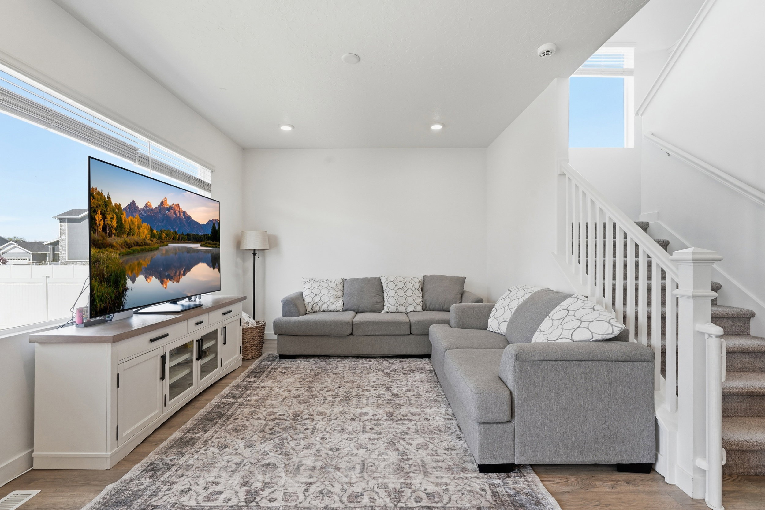 Bright living area featuring a large window, recessed lighting, wood-finish flooring, and a carpeted staircase with white balusters