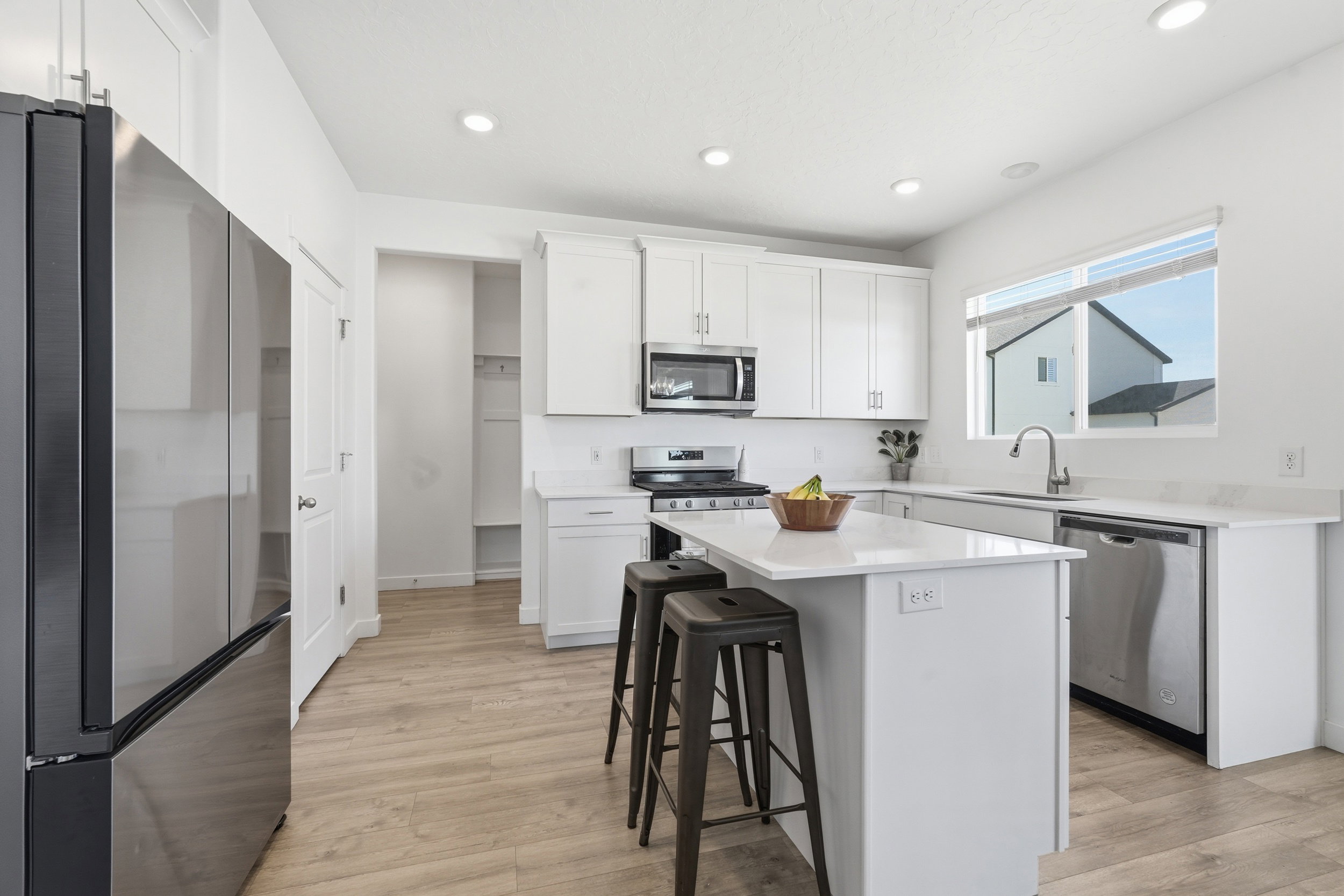 Modern kitchen featuring stainless steel appliances, white cabinetry, a central island with seating, recessed lighting, and wood-finish flooring