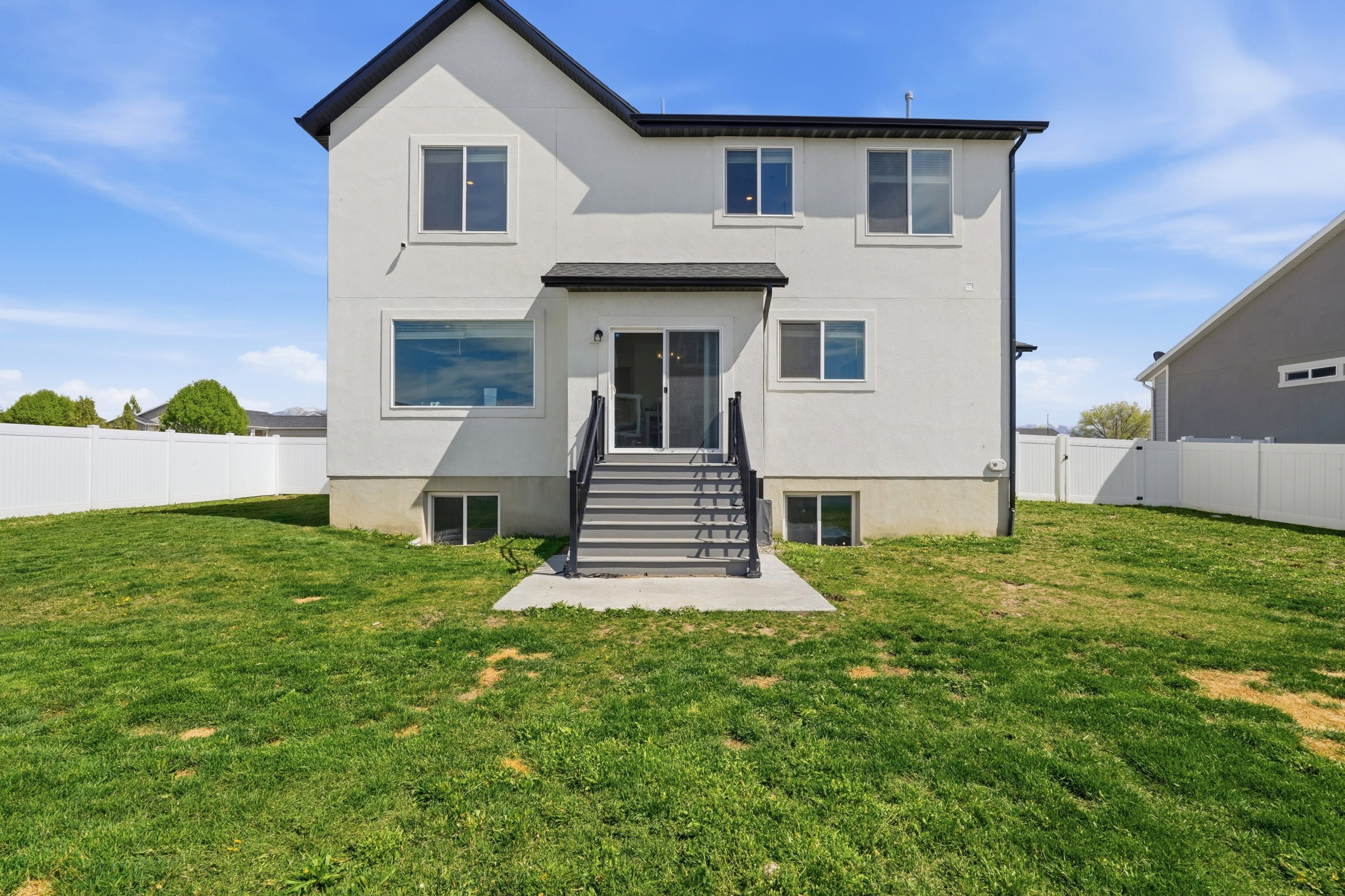 Expansive rear yard featuring a privacy fence, concrete patio, and exterior stairs with dark railings