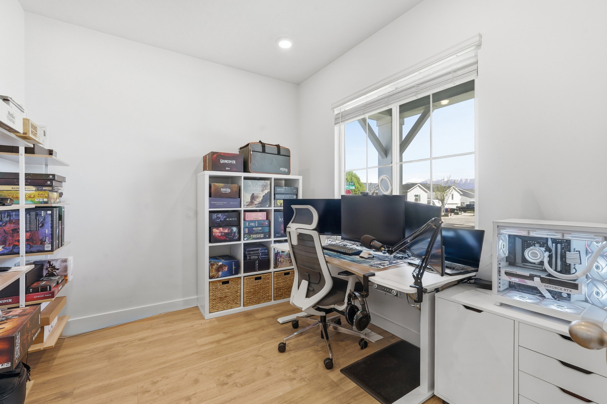 Spacious room featuring light wood-finish flooring, white walls, and a large window with white blinds