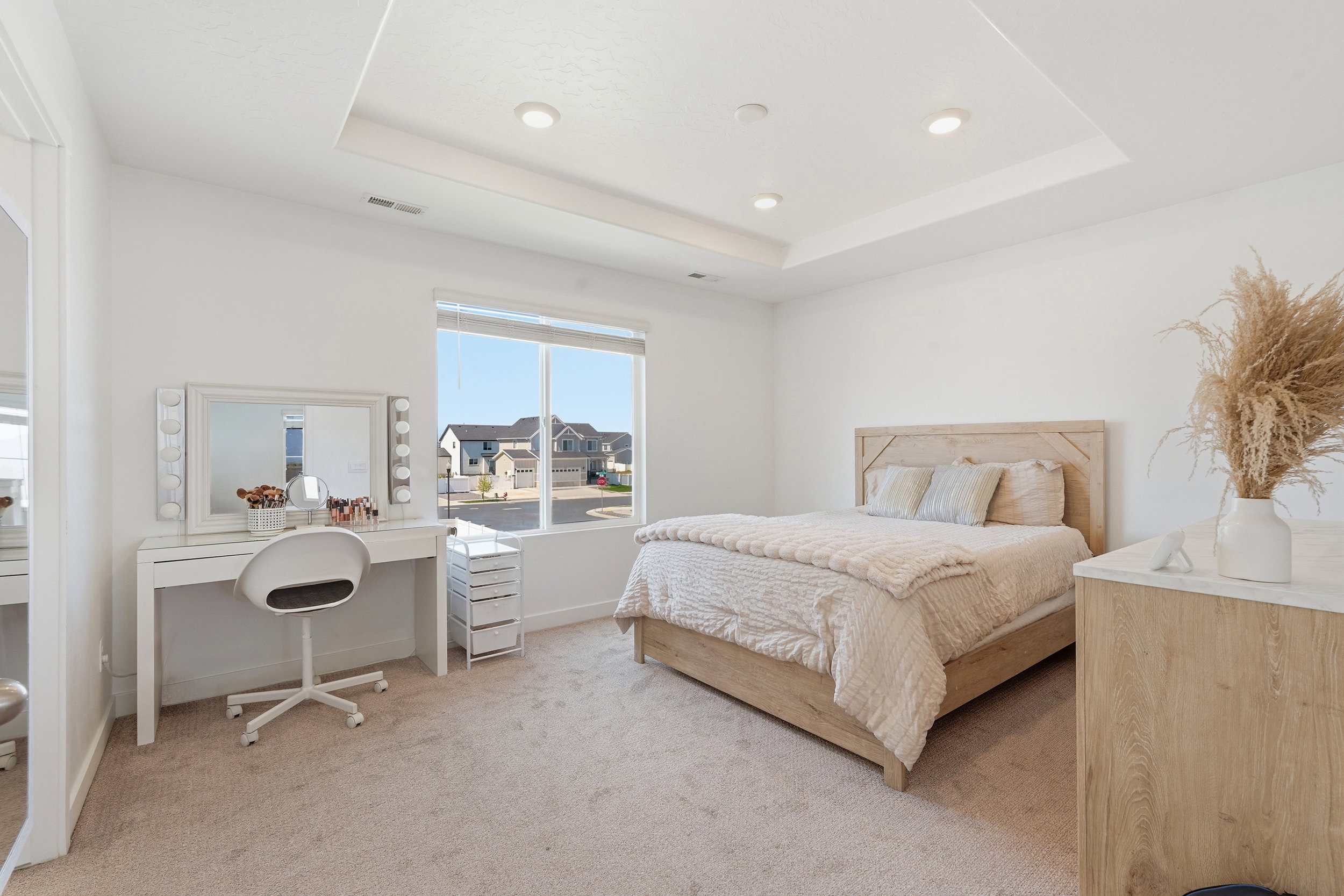 Spacious bedroom featuring light-toned carpeting, a tray ceiling with recessed lighting, and a large window