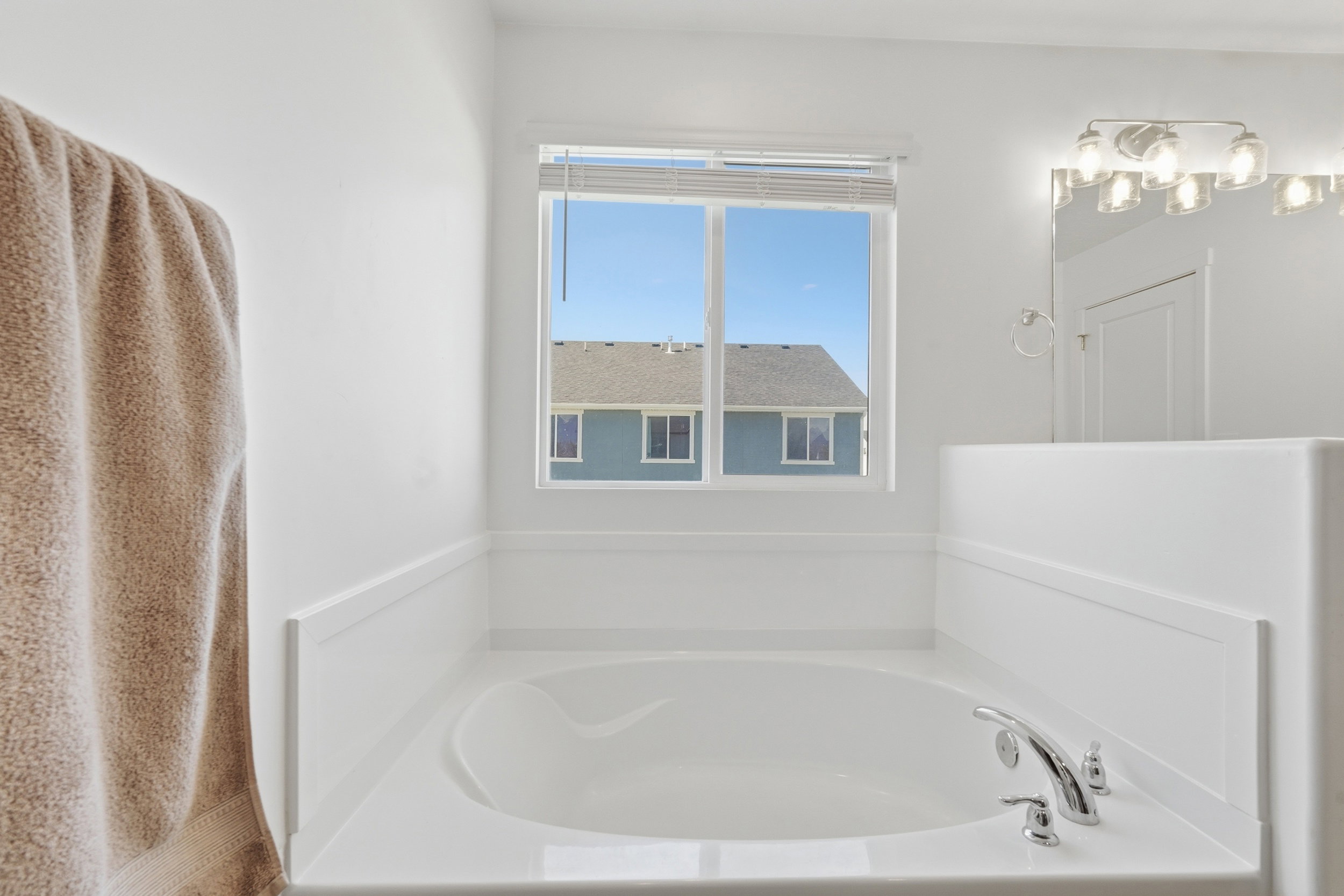 Built-in soaking tub with chrome fixtures, white wall paneling, and a window for natural light