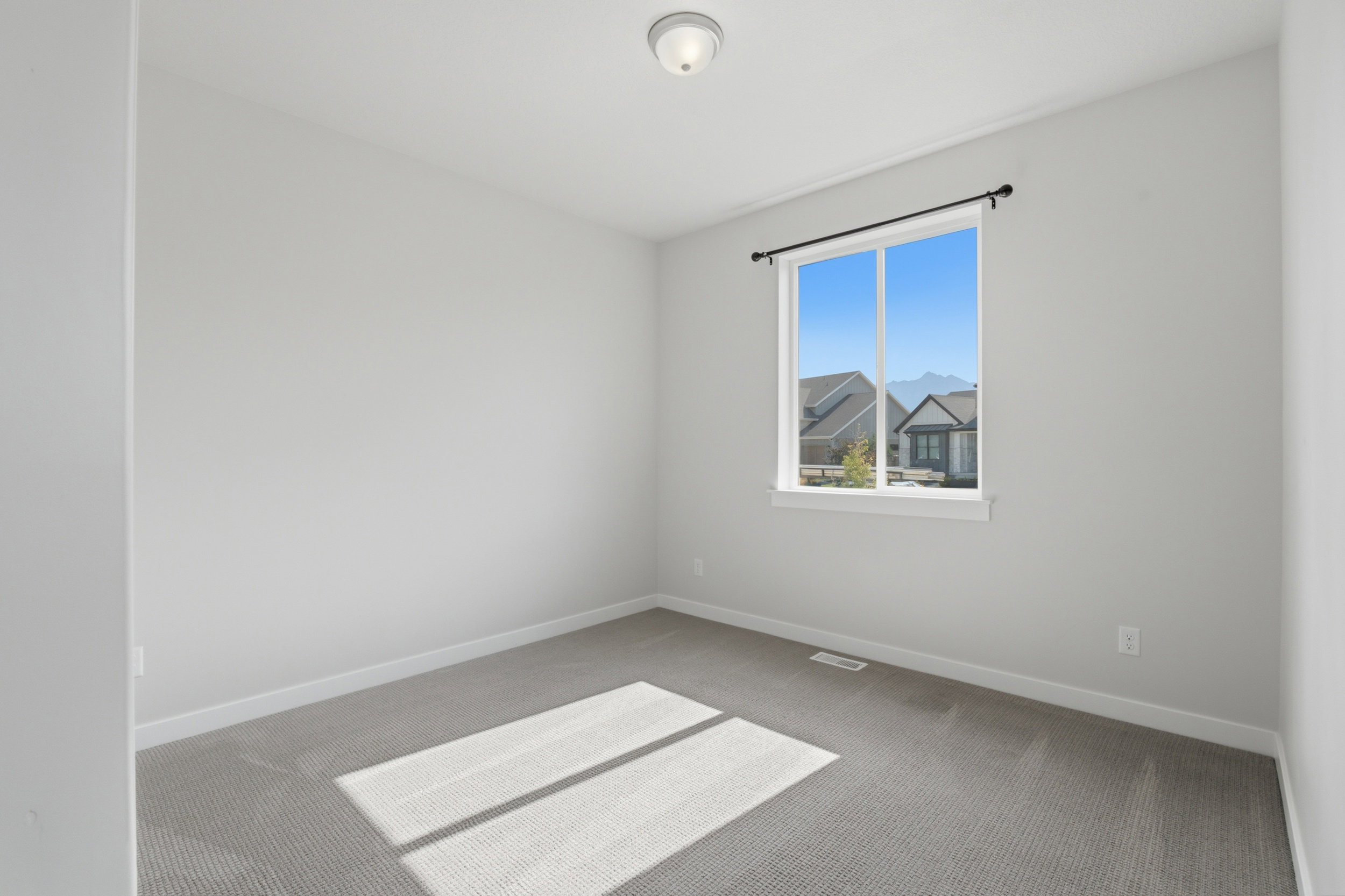 Windowed room featuring light gray walls, textured gray carpeting, white baseboards, and a semi-flush mount ceiling light