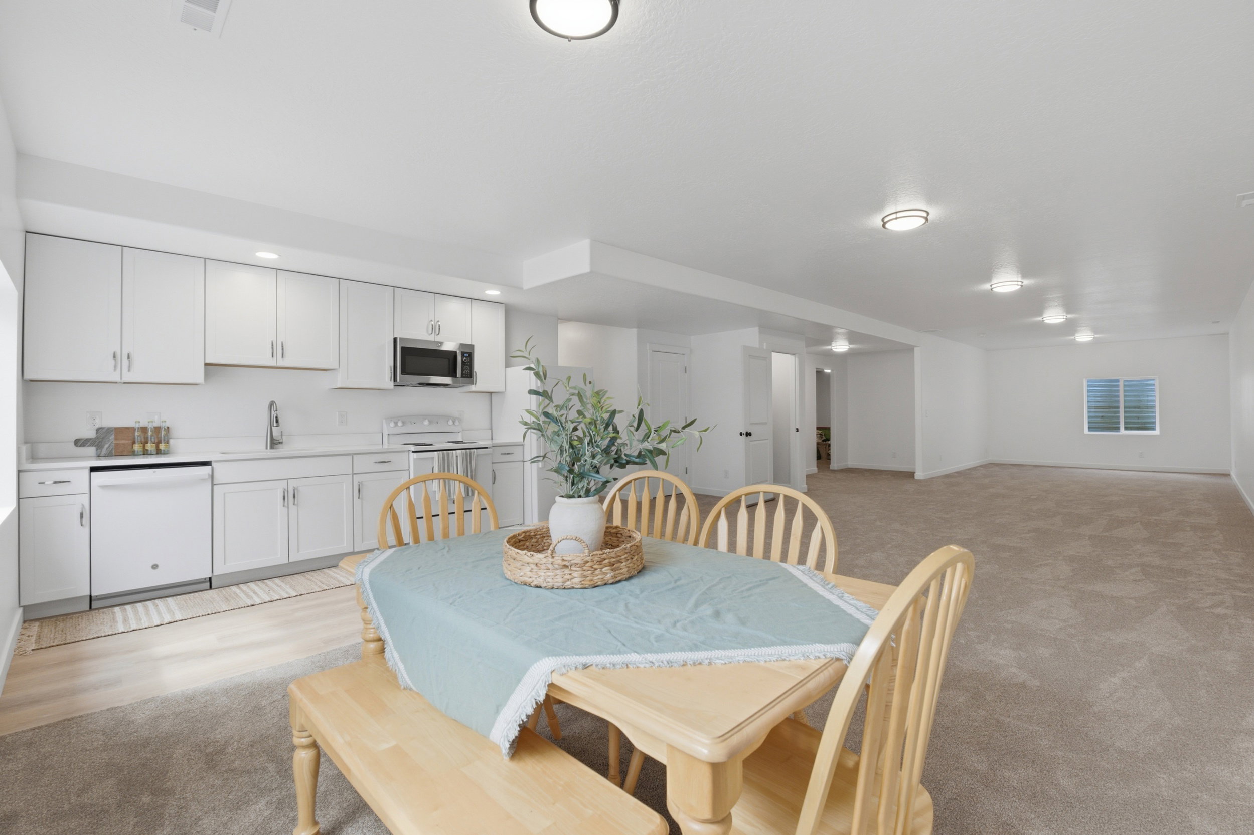 Open-concept living space featuring a full kitchen with white cabinetry, stainless steel appliances, and light countertops