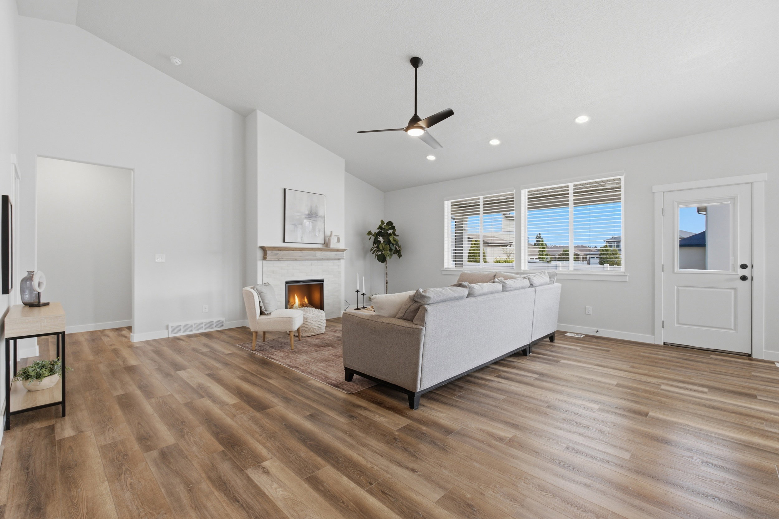Spacious living area featuring vaulted ceilings, wood-finish flooring, a stone-clad fireplace with wood mantel, large windows, and recessed lighting