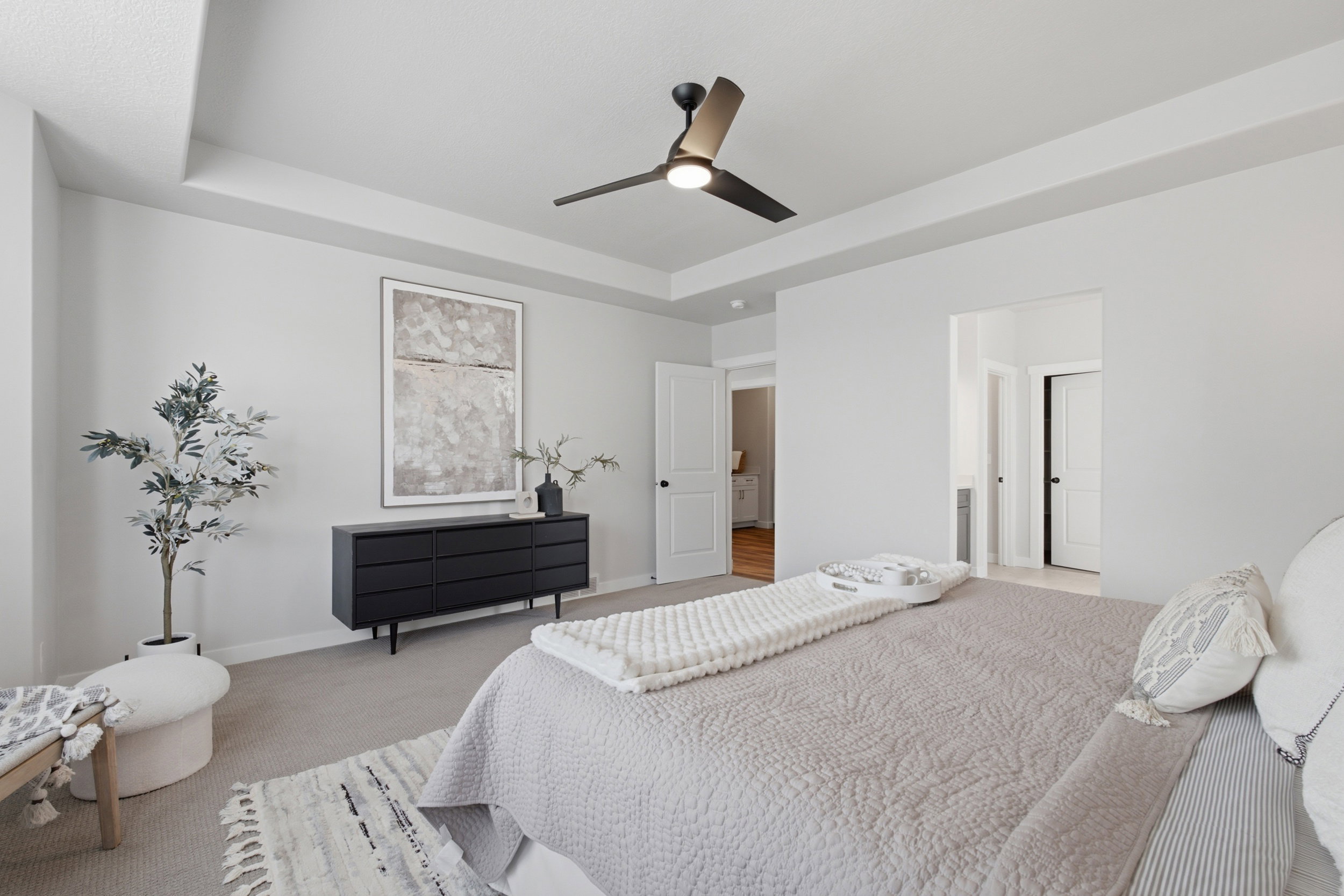 Spacious room with a tray ceiling, modern ceiling fan, light gray wall color, and plush carpet flooring