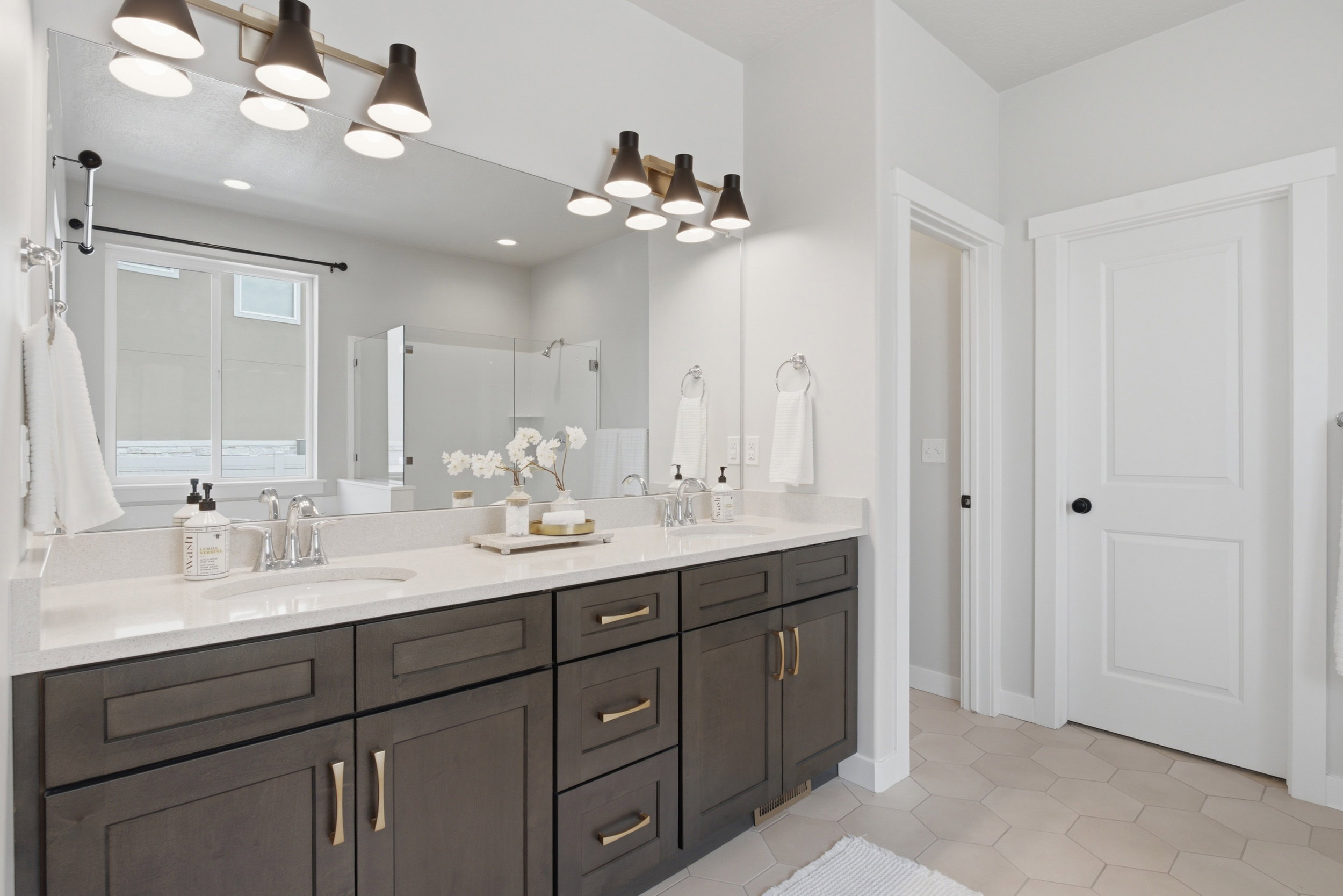 Dual sink vanity featuring dark wood-finish cabinetry, light-toned countertops, and contemporary light fixtures