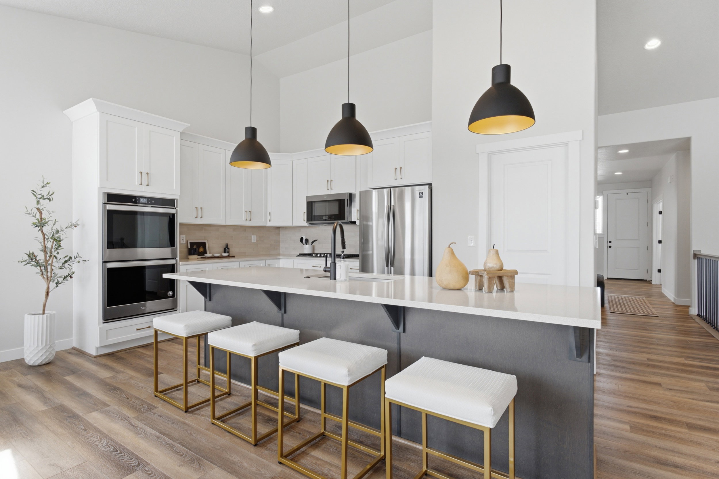 Kitchen featuring white upper cabinetry, a central island with a light-toned countertop, stainless steel double wall ovens, a tile backsplash, and wood-finish flooring