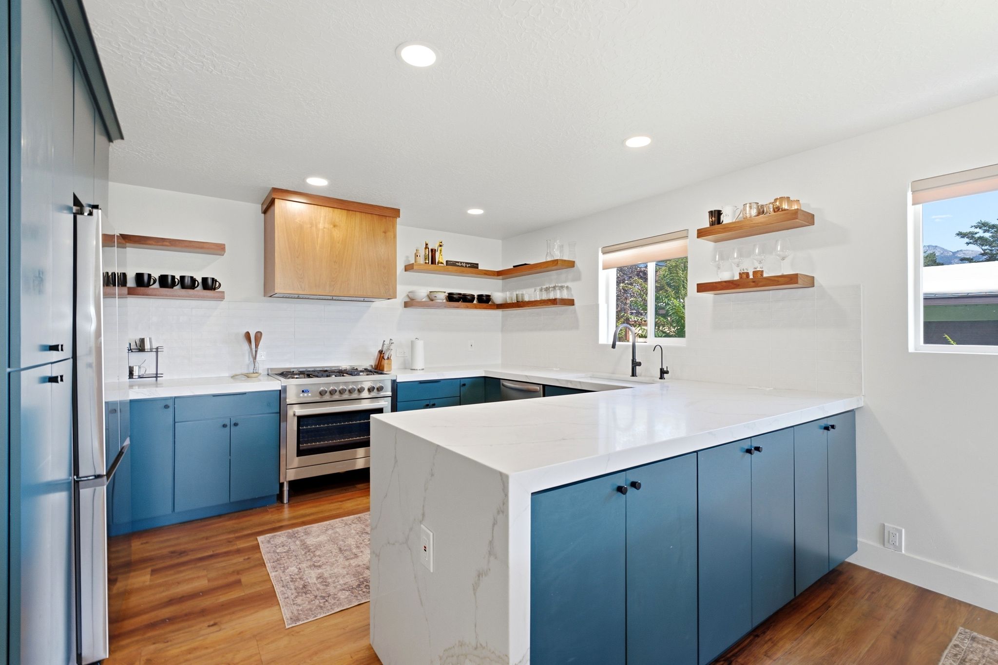 Modern kitchen featuring a waterfall island with a light-toned countertop, a stainless steel refrigerator, and wood-finish flooring