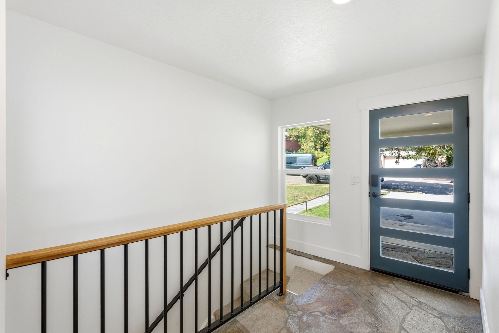 Entryway featuring a modern paneled door with glass inserts, a large window, a wood handrail with black metal balusters, and flagstone flooring