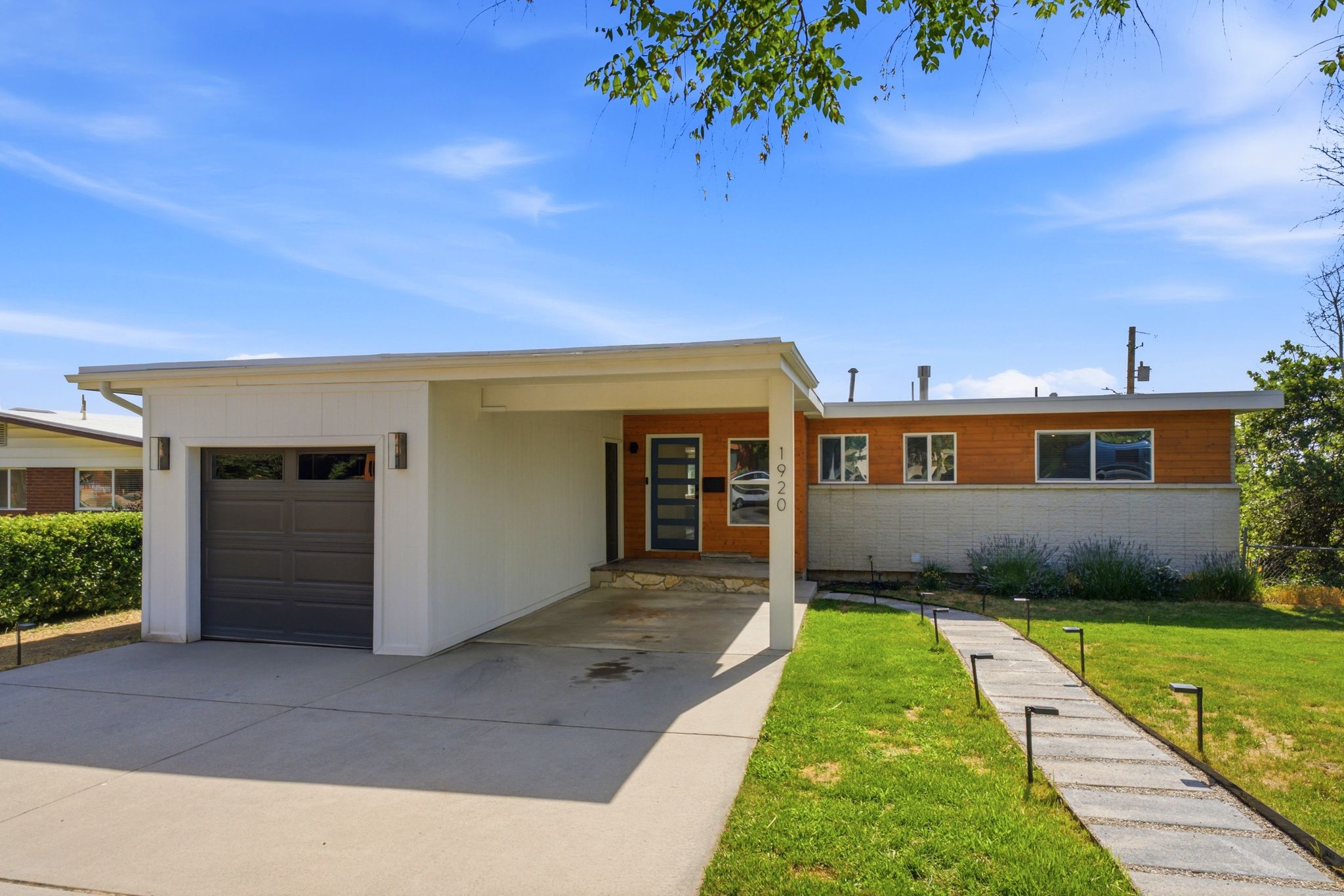 Modern exterior with wood-finish siding, a dark gray garage door, and a covered carport