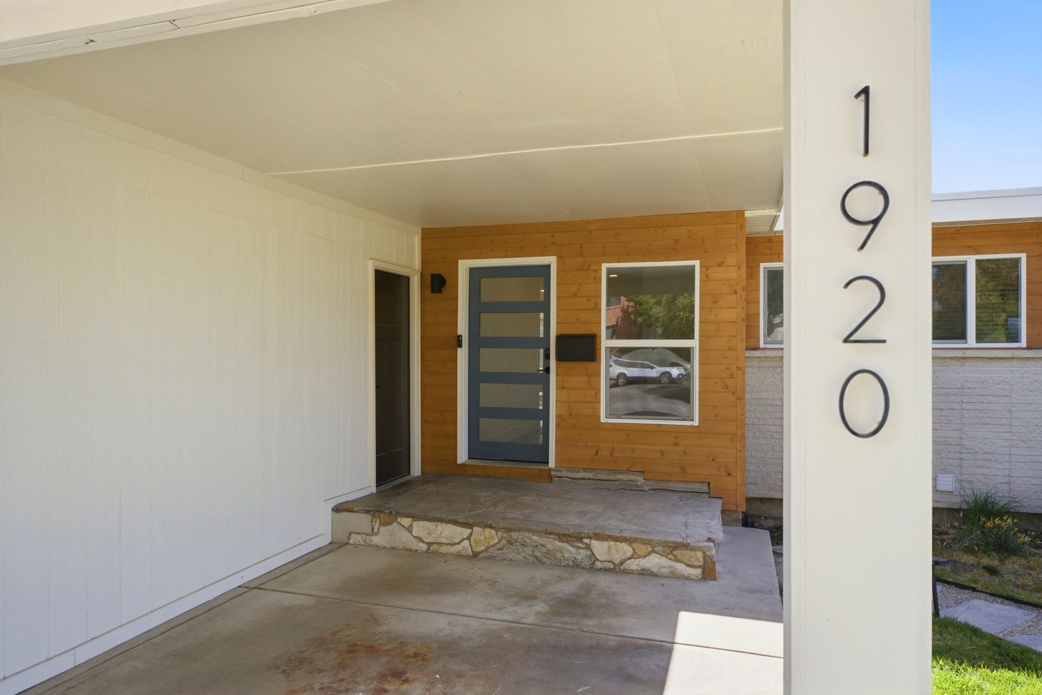 Contemporary entry with wood paneling, a modern glass-paneled door, and a stone-clad porch