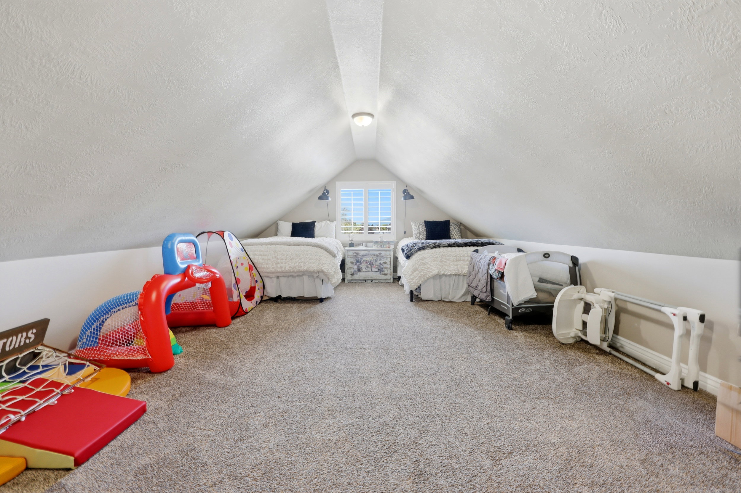 Attic room featuring sloped ceilings, light-colored textured walls, and a recessed window with white louvered shutters