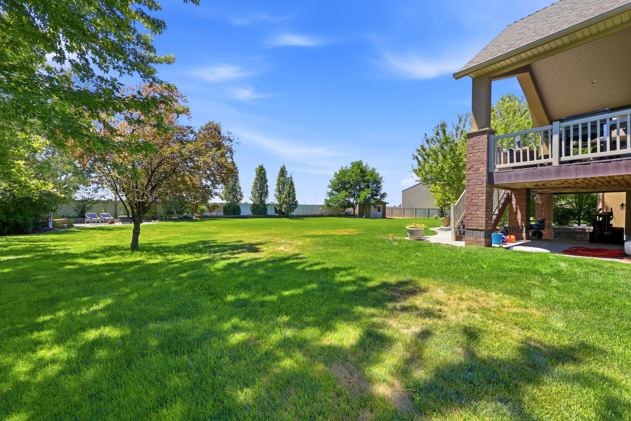 Spacious green lawn with mature trees and a multi-level deck featuring a stone column and wood railing